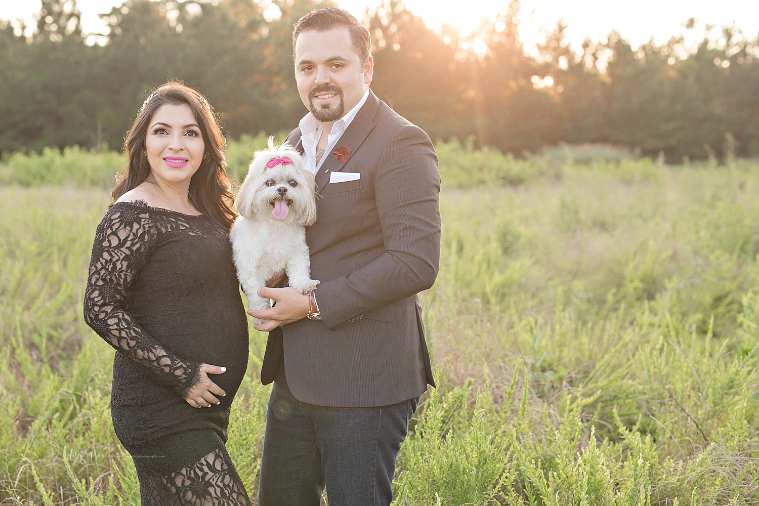  Image of a pregnant Latina woman, wearing a black lace dress, standing with her husband who is holding their little dog.&nbsp; 