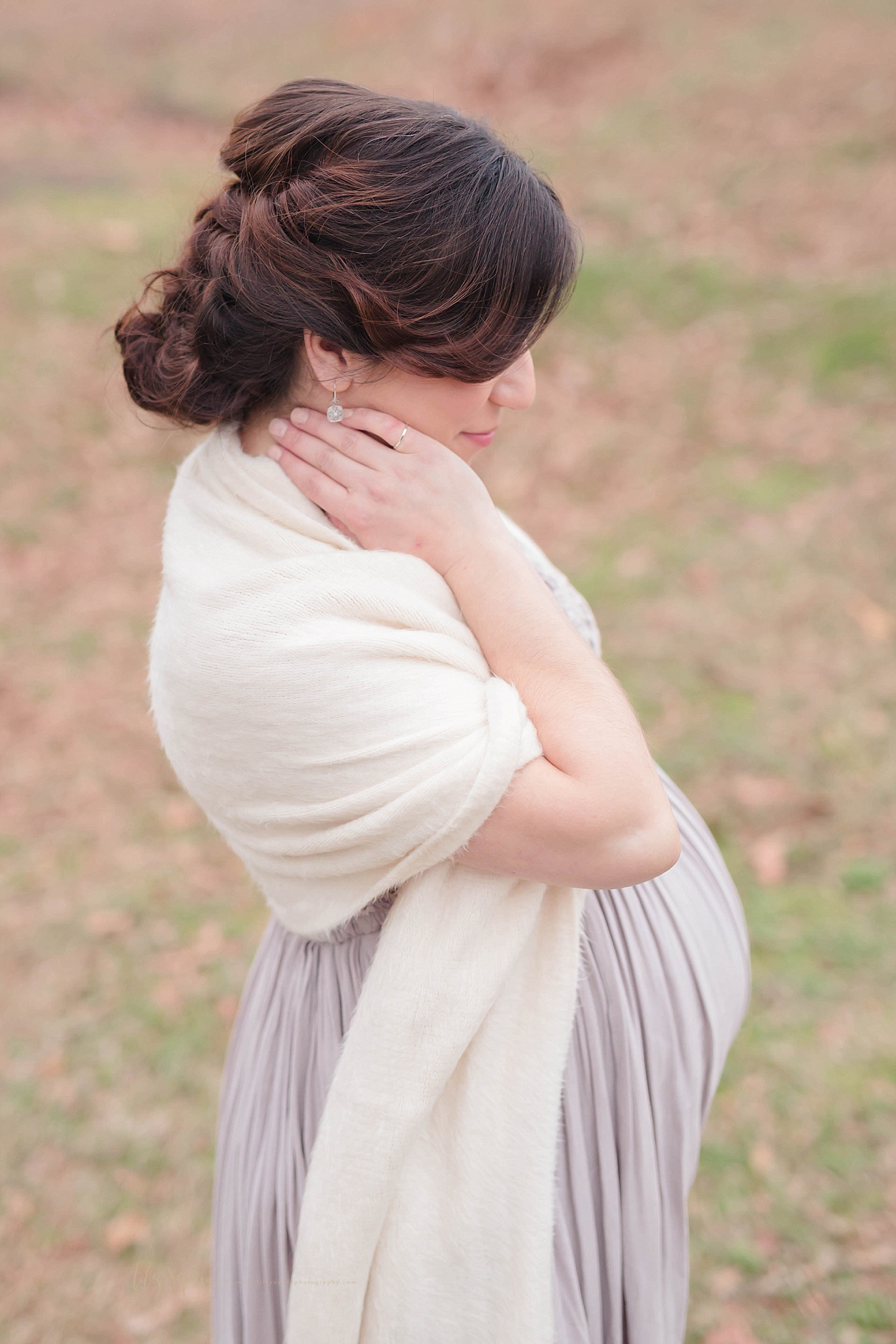  Atlanta mother-to-be with braided auburn hair wears a taupe dress.  She has an off-white shawl draped over her shoulders. with her right arm bent and her right hand resting on her neck.   