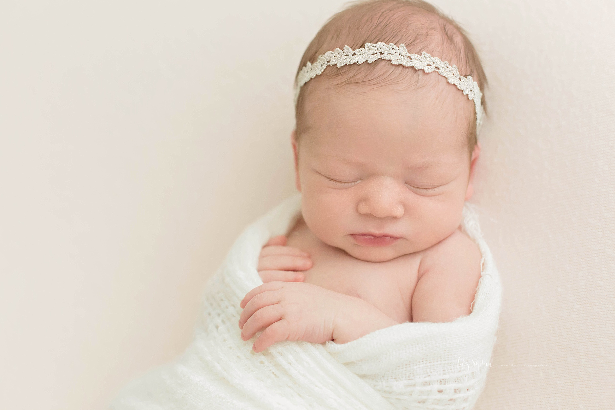  Image of a sleeping, newborn, baby, girl, with a leaf headband, wrapped up, with her hands sticking out. 