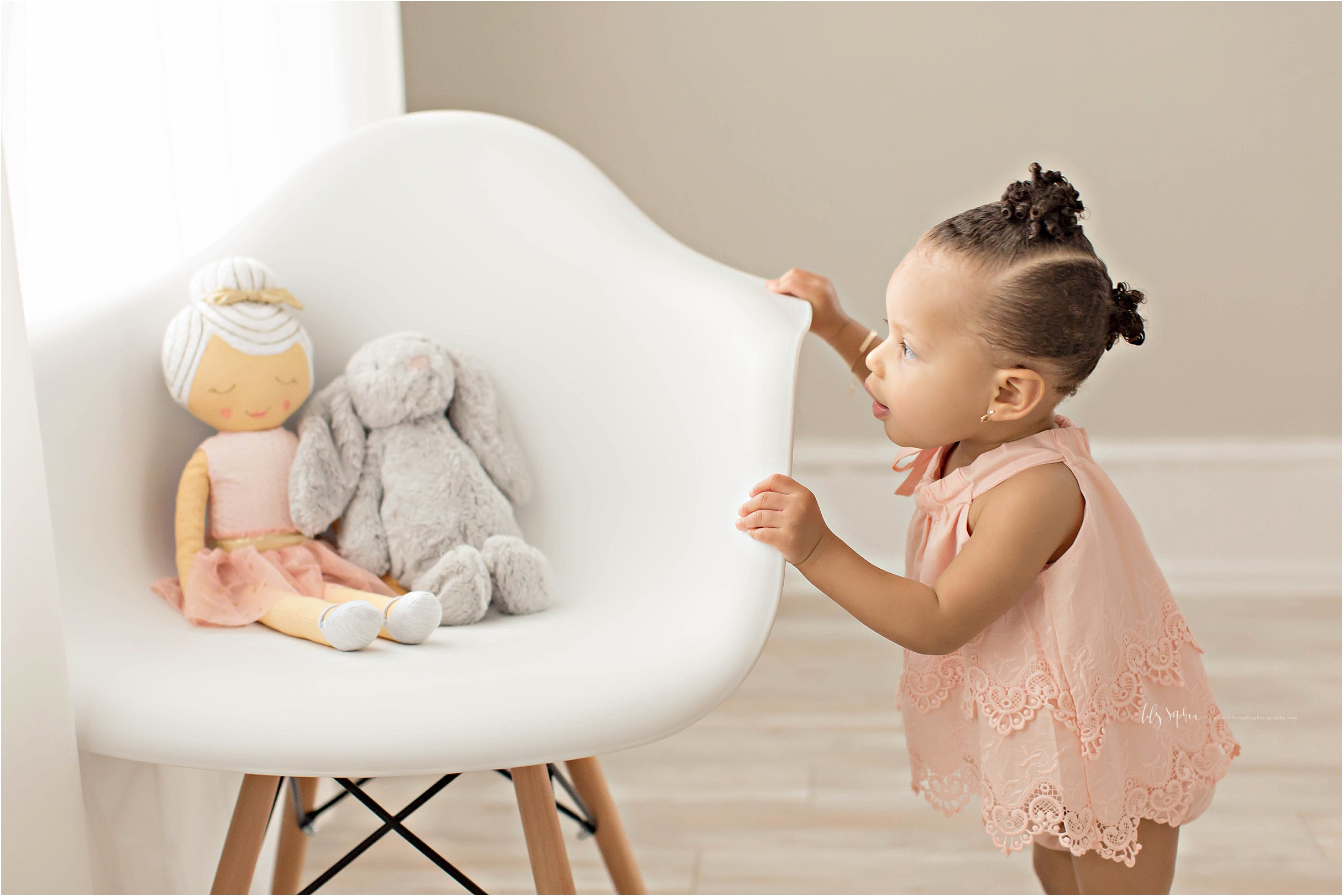  Image of a baby, one year old, African American, girl, looking at her lovey's sitting in a chair.&nbsp; 
