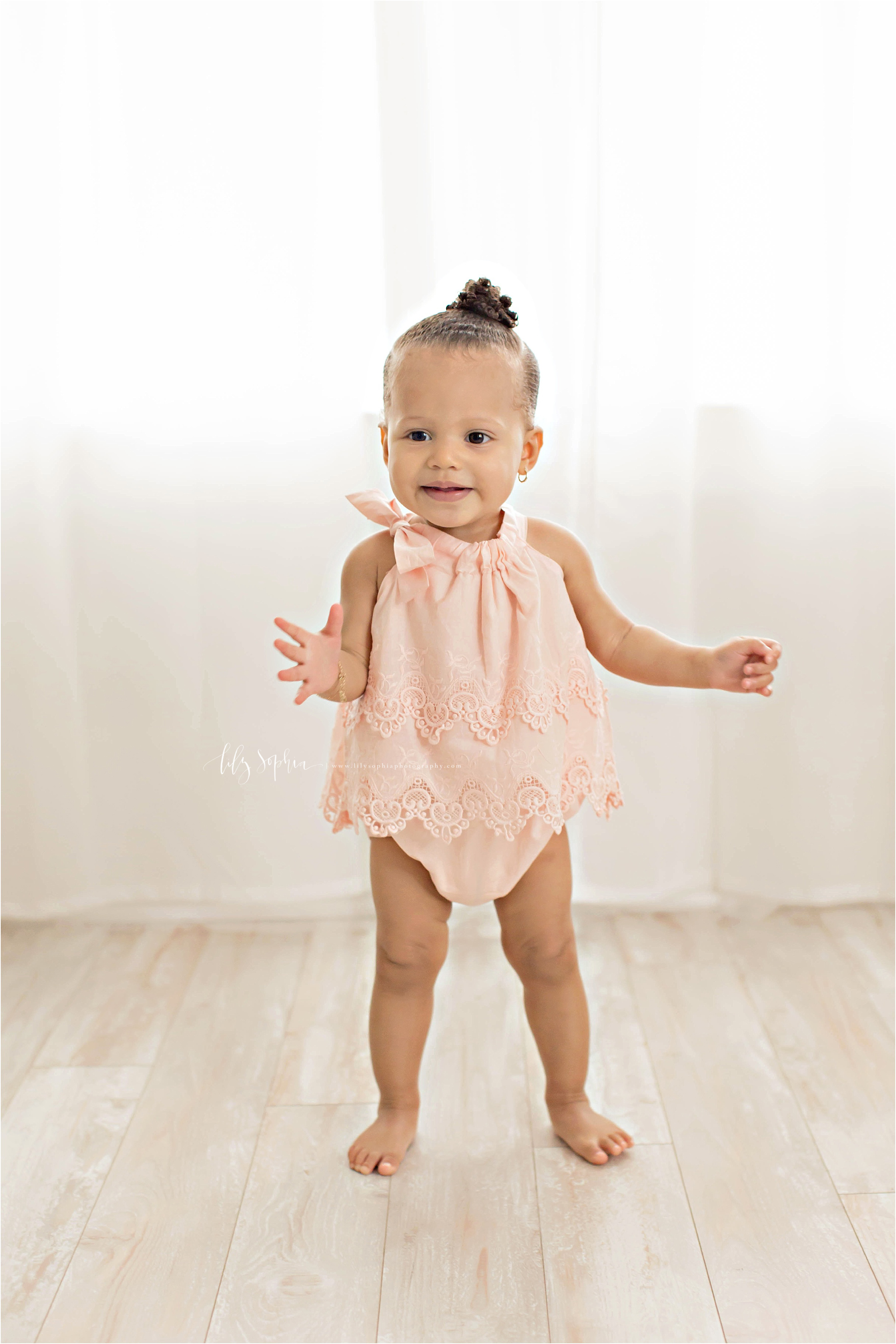  Image of a one year old, baby, African American, girl, standing in a peach jumper and smiling.&nbsp; 