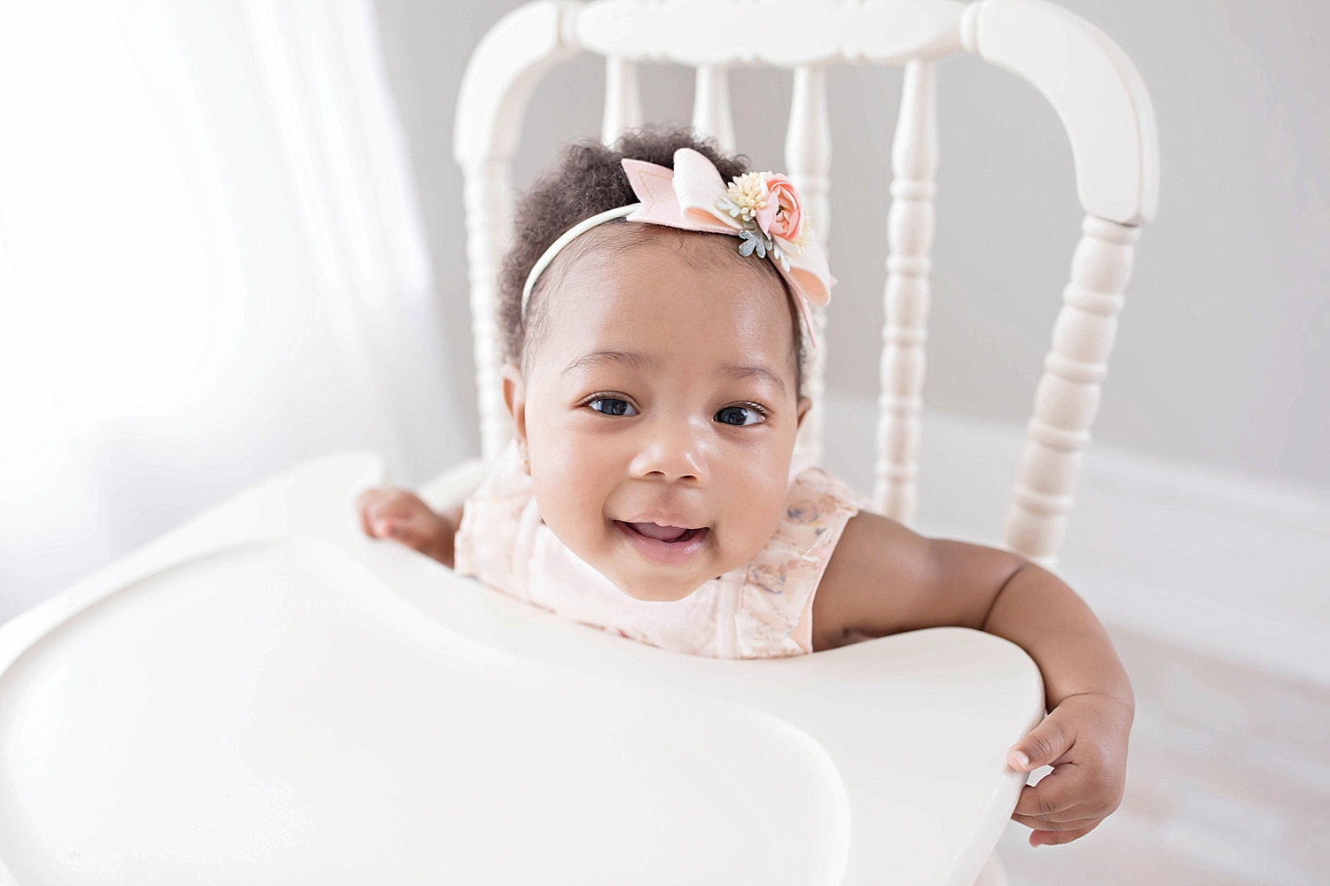  Image of a smiling, African American, toddler girl, with a pink, flower, bow headband in her hair, sitting in an antique wooden highchair.&nbsp; 