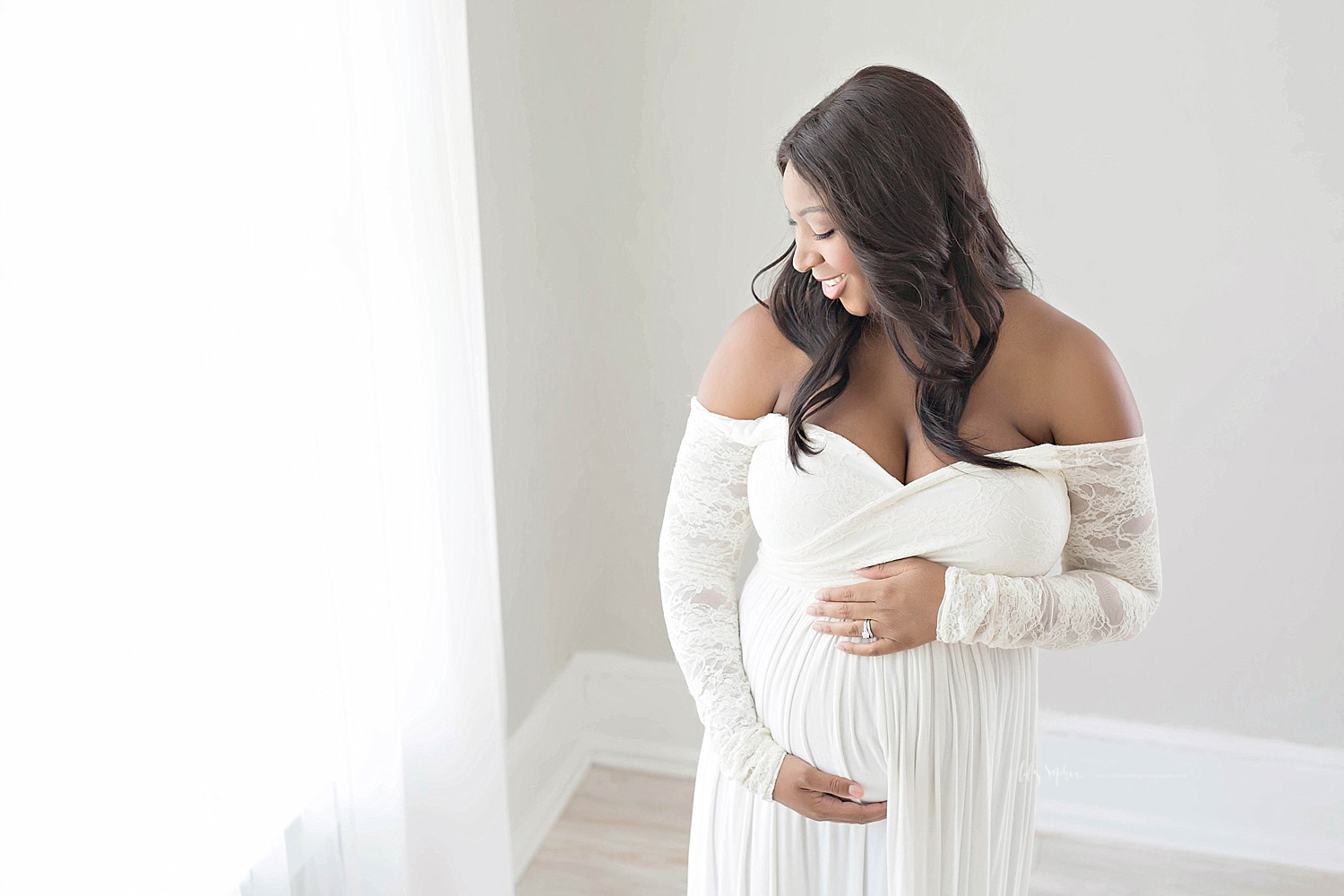  Image of a pregnant African American woman, smiling, in a cream, off the shoulder dress with lace sleeves.&nbsp; 