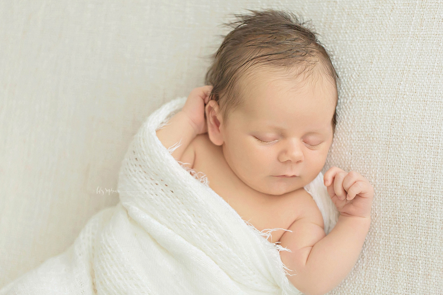  Image of a sleeping, newborn, baby, boy, wrapped in a waffle weave, white blanket, with his hands by his head.&nbsp; 