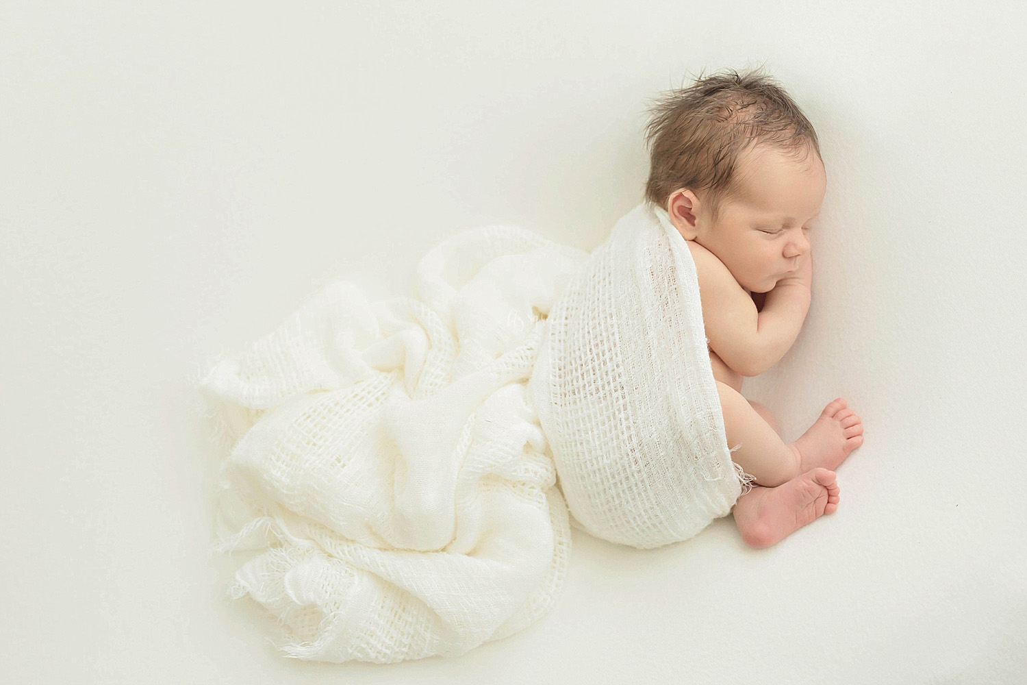  Image of a baby, newborn, boy, sleeping on his side, partially wrapped up in a cream blanket.&nbsp; 