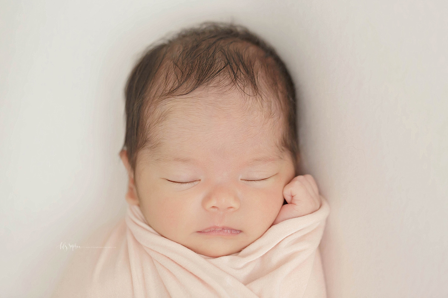  Image of a sleeping, newborn, baby, girl, wrapped up in alight pink blanket with her hand under her cheek.&nbsp; 