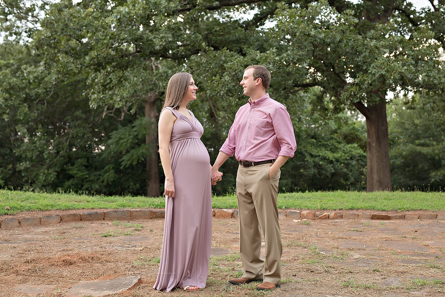  Image of a pregnant woman,&nbsp; wearing an empire waist, light purple, maxi dress and facing her husband and holding his hand&nbsp; 
