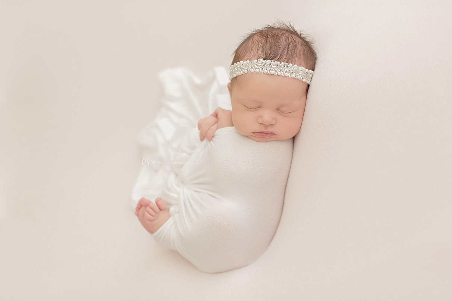  Image of a sleeping, newborn, baby, girl, on her back, wrapped in a white blanket with her toes and hands sticking out and wearing a white lace headband on her head.&nbsp; 