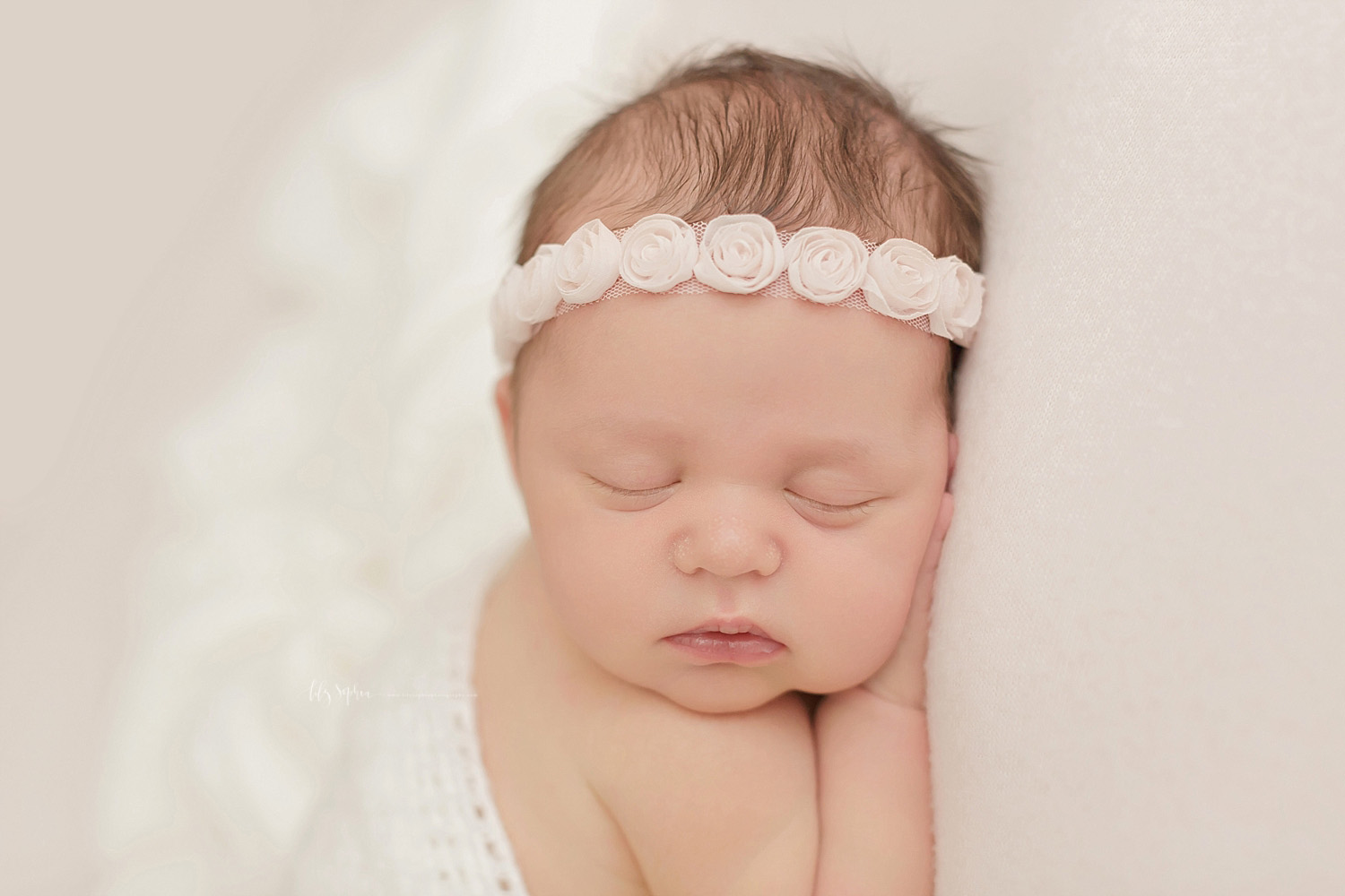  Up close image of a sleeping, newborn, baby, girl, with a rosebud headband in her hair sleeping on her cheek.&nbsp; 