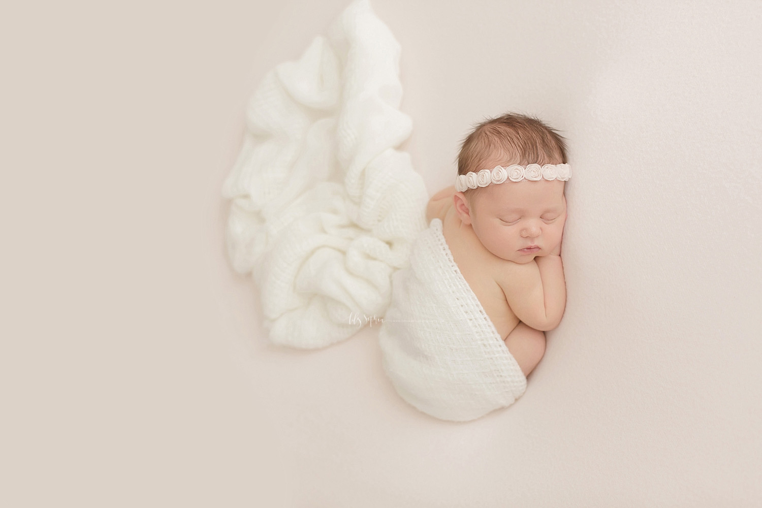  image of a sleeping, newborn, baby, girl, on her stomach, partially wrapped with a waffle weave, cream, blanket, with a rosebud headband in her hair.&nbsp; 