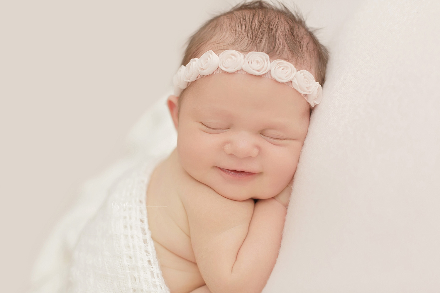  Close up image of a newborn, baby, girl, grinning in her sleep, with her hands tucked under her chin.&nbsp; 
