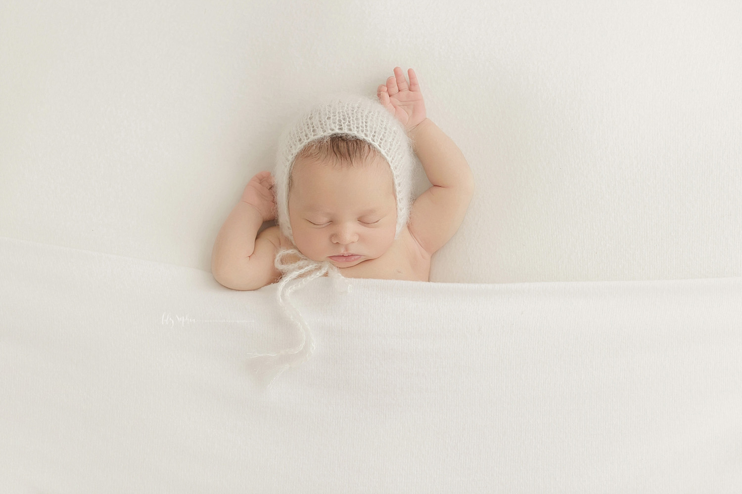  Image of a newborn, baby, girl, with a white bonnet on her head, sleeping on her back, with her arms stretched out.&nbsp; 
