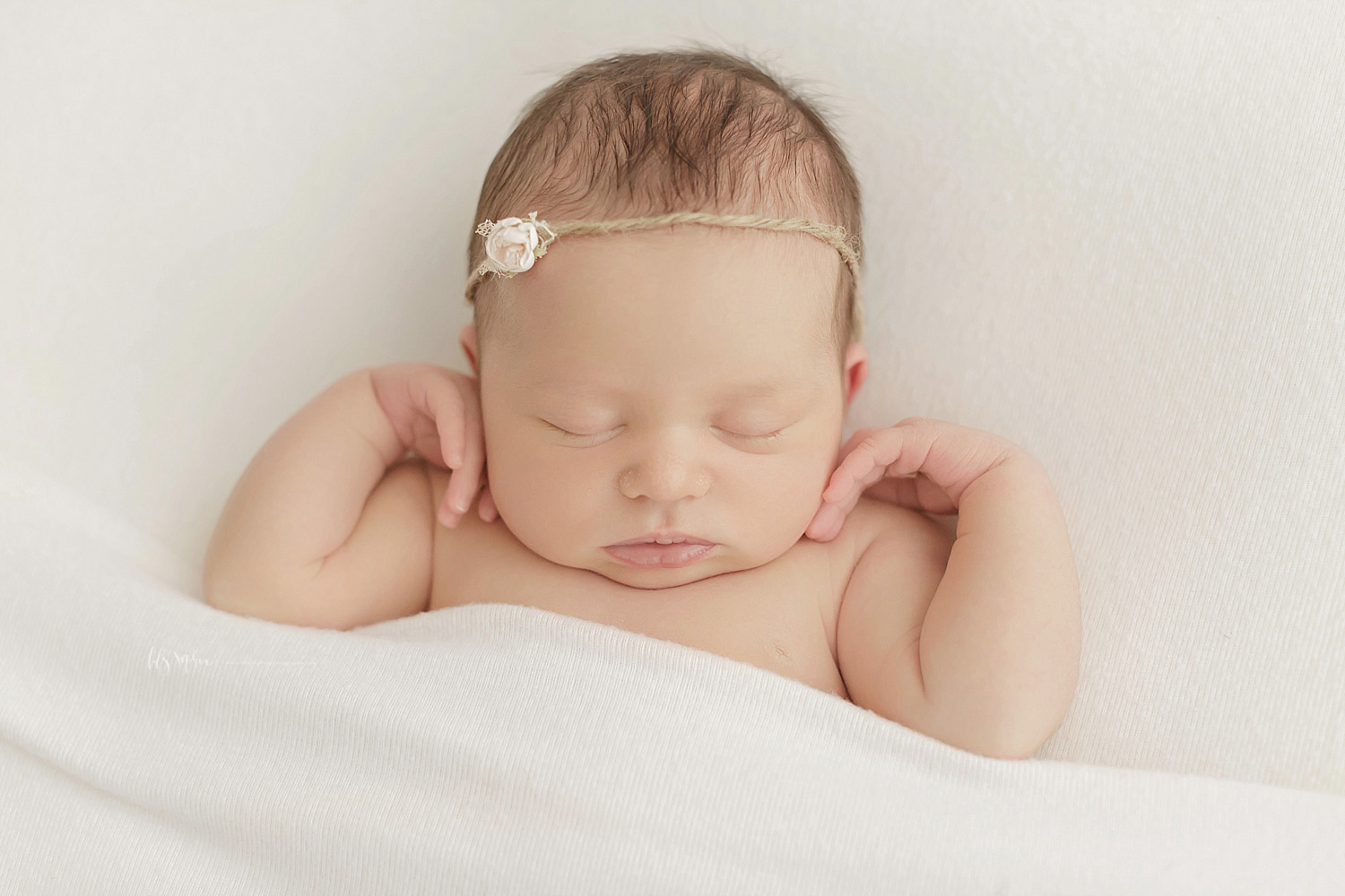  Image of a sleeping, newborn, baby, girl, on her back, with her hands tucked under her ears, wearing a cream rosebud tieback in her hair.&nbsp; 