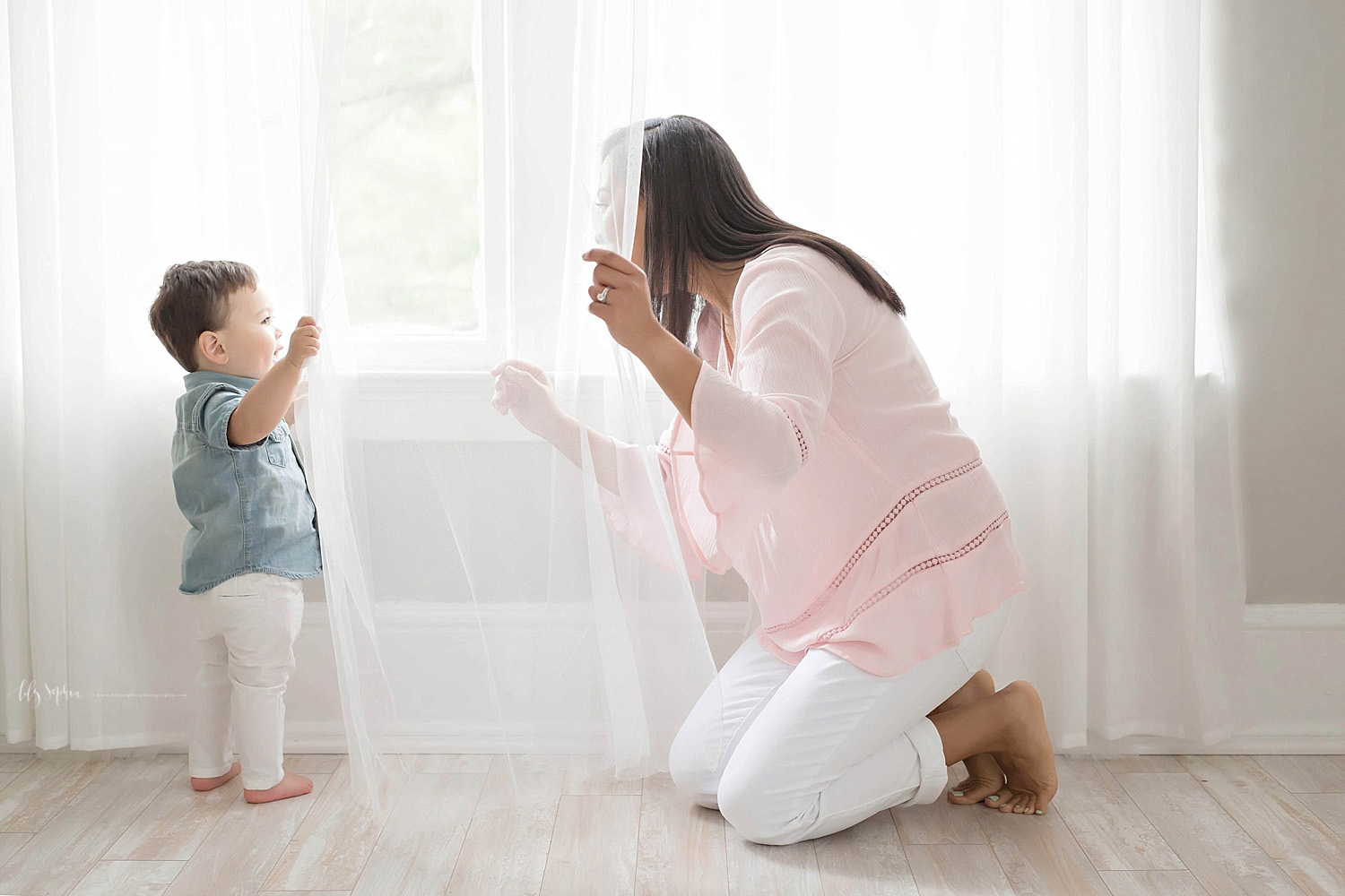  Image of mother and son, playing peek-a-boo in front of a window.&nbsp; 
