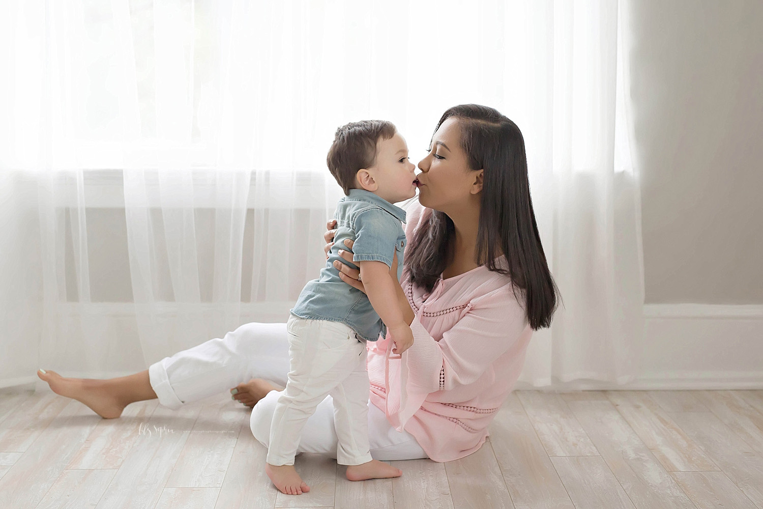  Image of a mother, sitting on a the floor, while she kisses her toddler son.&nbsp; 