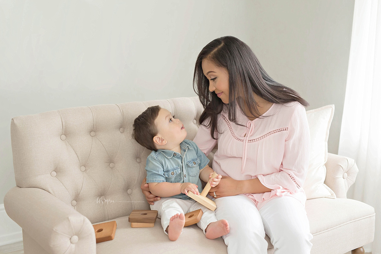  Image of a mother and her son, sitting on a couch, looking at each other while he plays with a wooden stacking toy.&nbsp; 