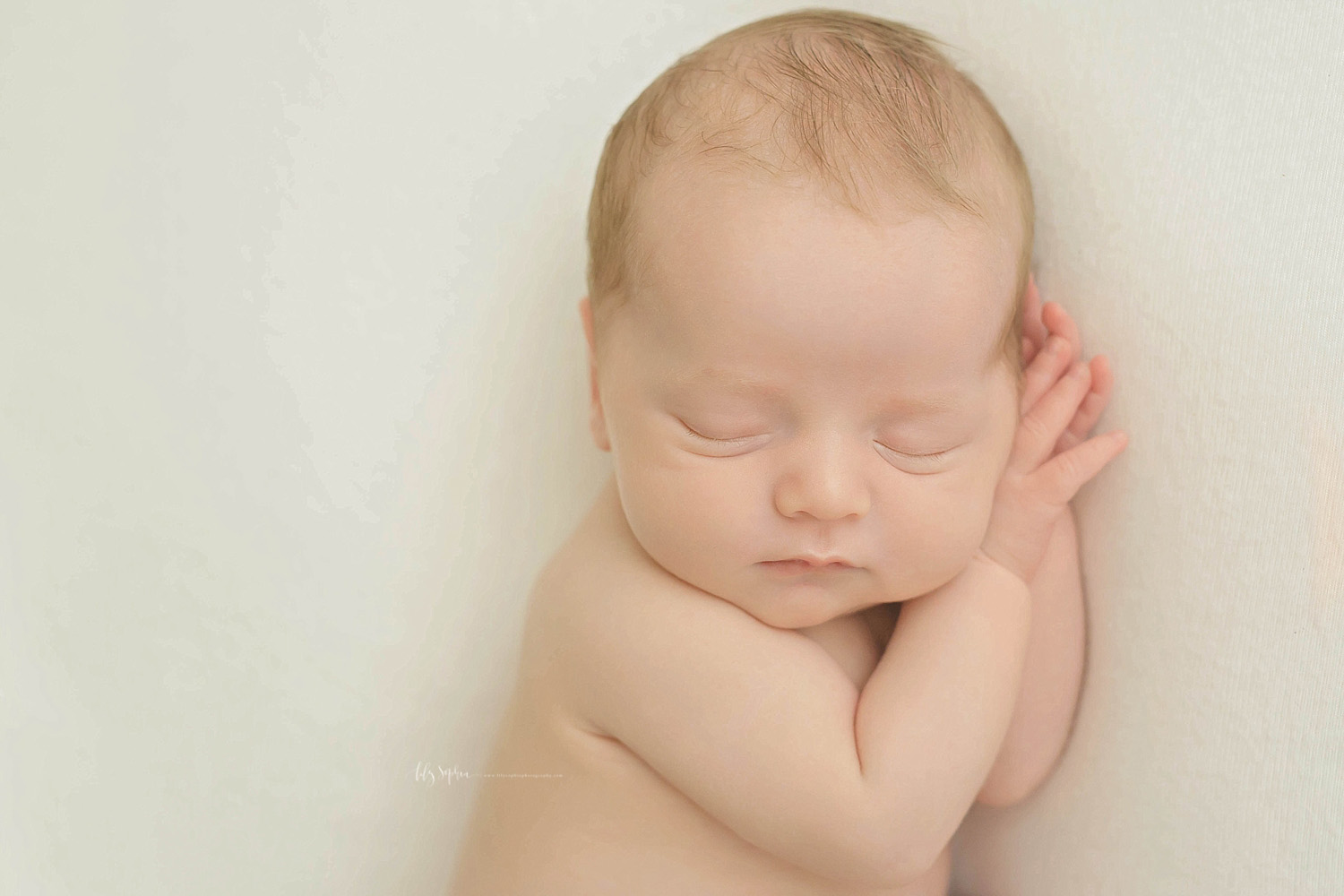  Image of sleeping, newborn, baby boy, sleeping on his side, with his hands tucked under his chin.&nbsp; 