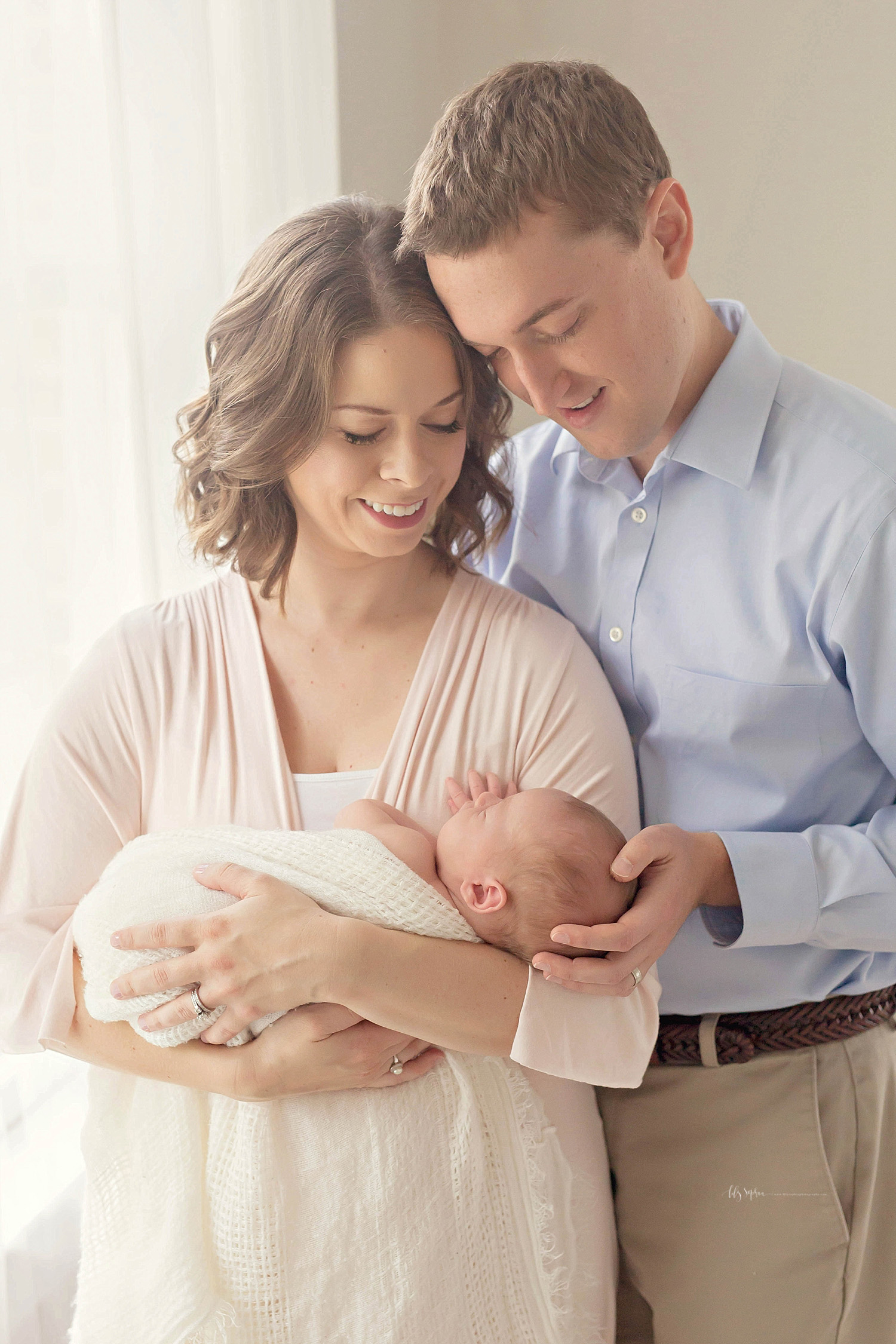  Image of a mother smiling down at her newborn son in her arms, while her husband places his hand on his son's head and smiles down at him.&nbsp; 