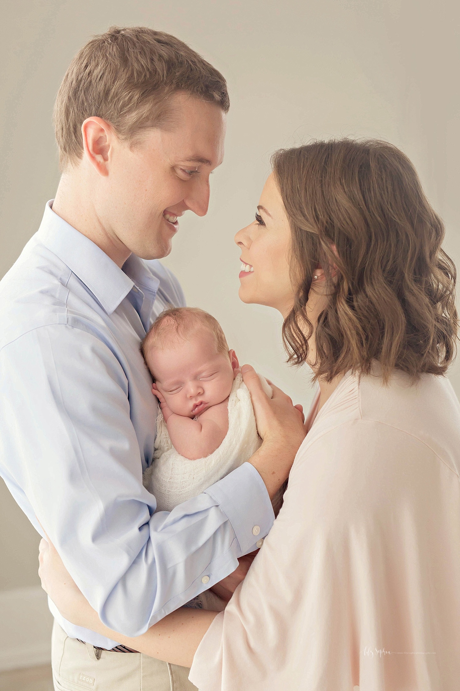  Image of a father, holding his sleeping, newborn son to his chest, while he smiles at his wife and she smiles back at him.&nbsp; 