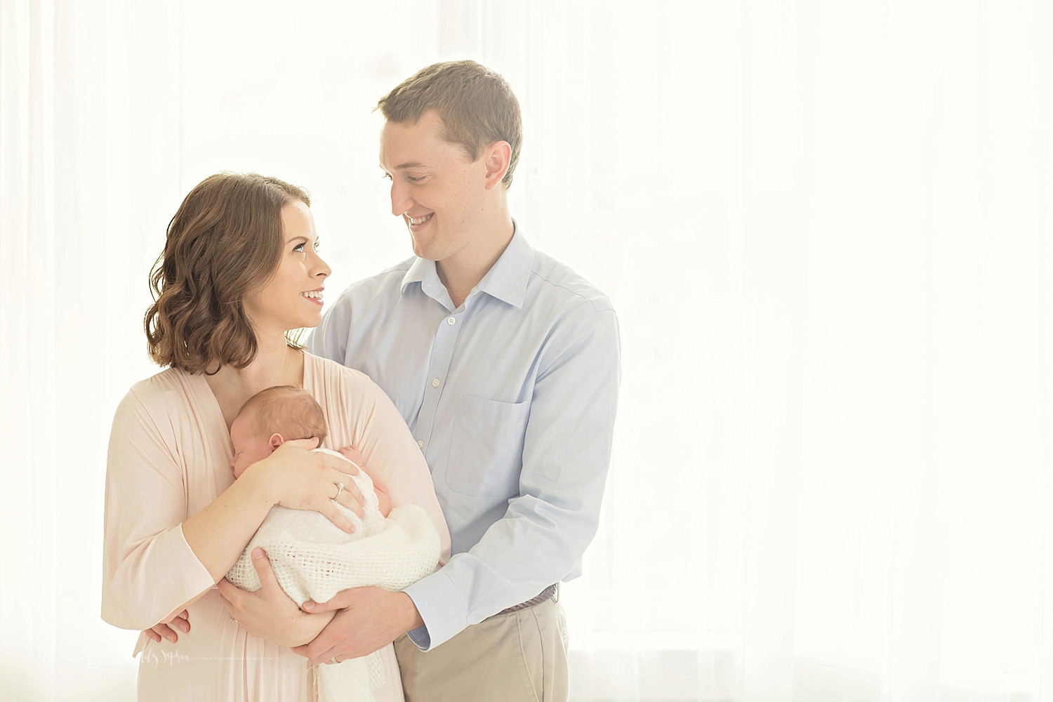  Image of new parents, looking at each other and smiling, while their sleeping newborn, son is cuddled to his mother's chest&nbsp; 