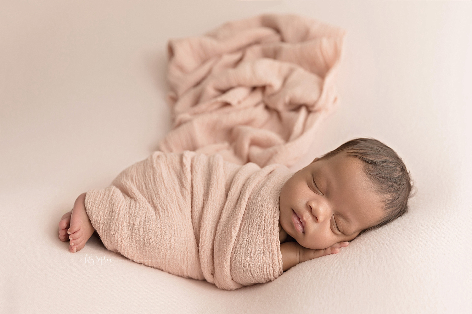  Image of a sleeping, African American, baby girl, sleeping on her side, wrapped up in a pink wrap with her feet sticking out and her hand under her chin.  