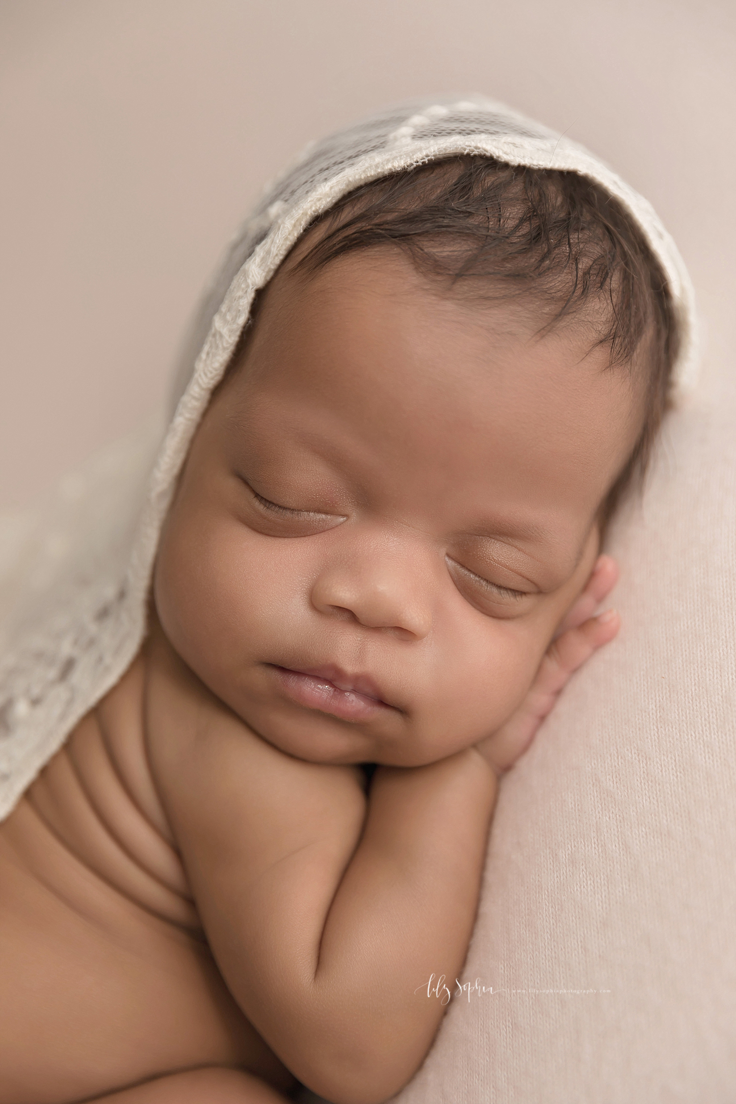  Close up image of a sleeping, baby, girl, on her stomach, partially covered with a blanket, and with her hand under her chin. 