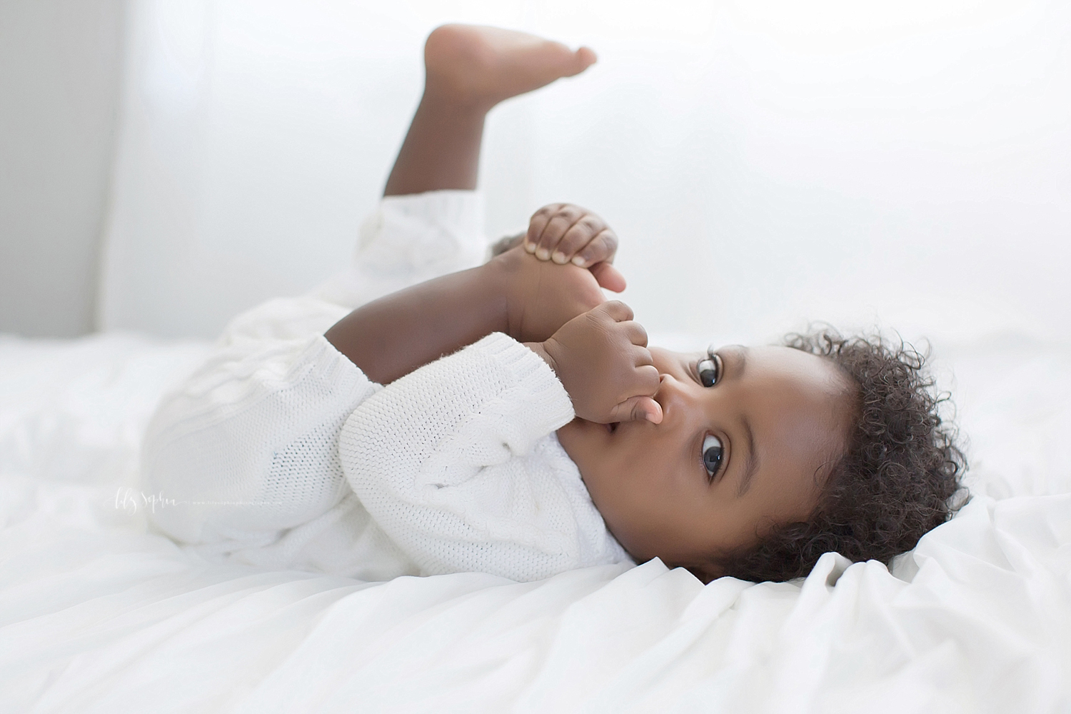  Image of a African American, baby, boy, eating his toes and looking at the camera.  