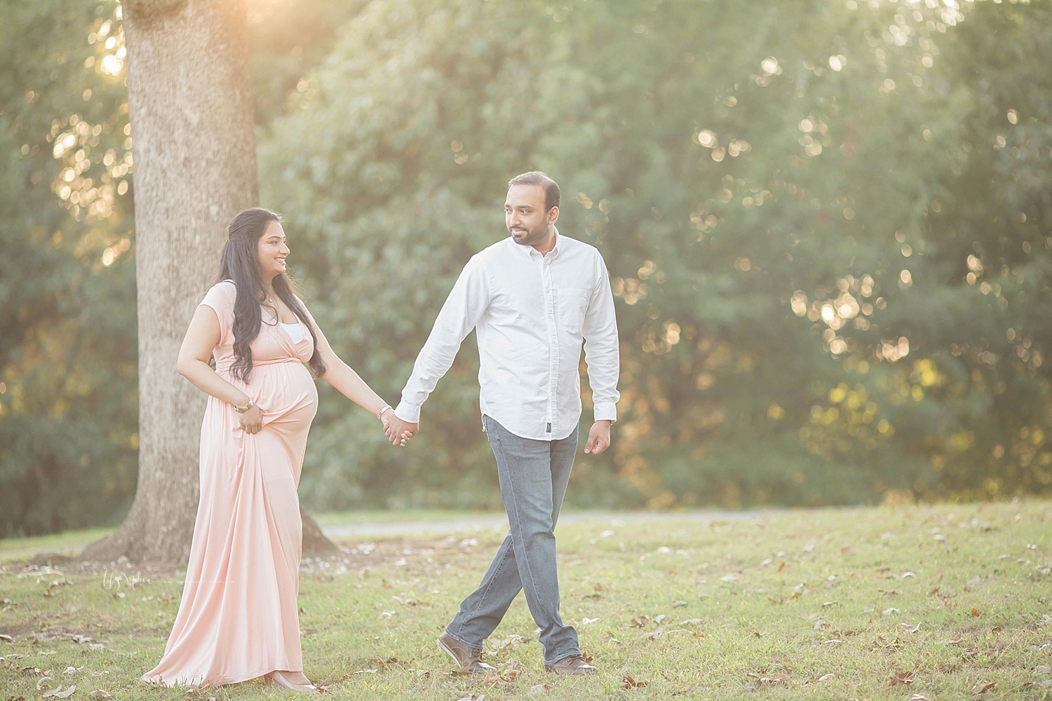 Image of a pregnant couple, walking through a sunlight, park, in Atlanta, taken by Lily Sophia Photography. 