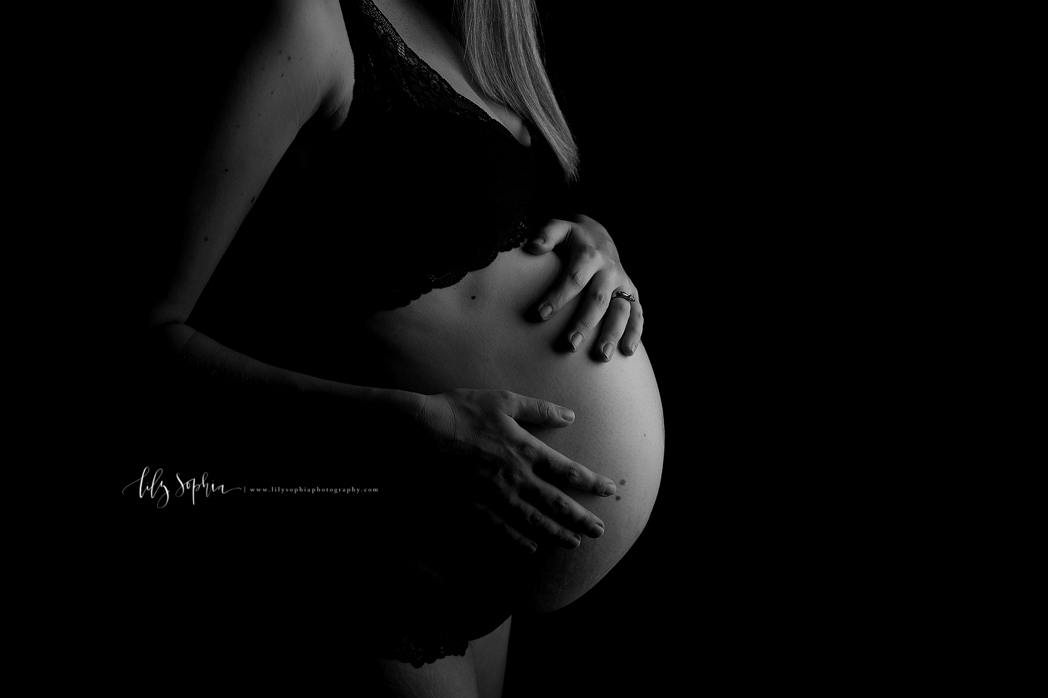  Black and white editorial maternity image with rim lighting of 38 weeks pregnant woman’s hands on bare belly in the intown Atlanta studio of Lily Sophia Photography. 