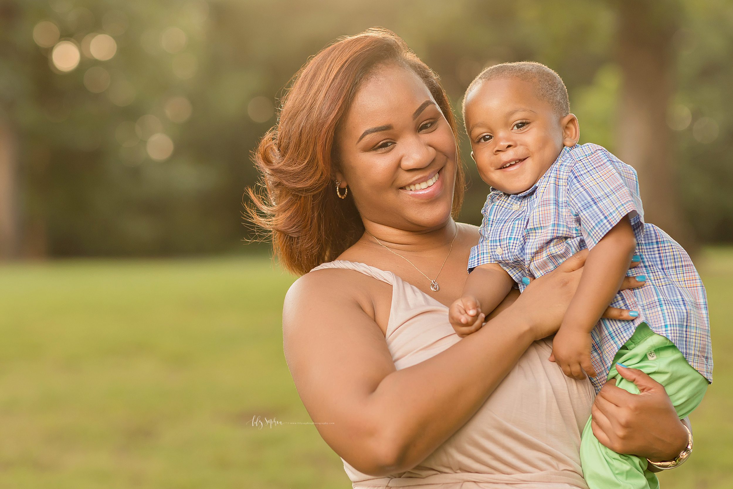  Happy African American mom with auburn hair holding her two year old son in an Atlanta park at sunset. 