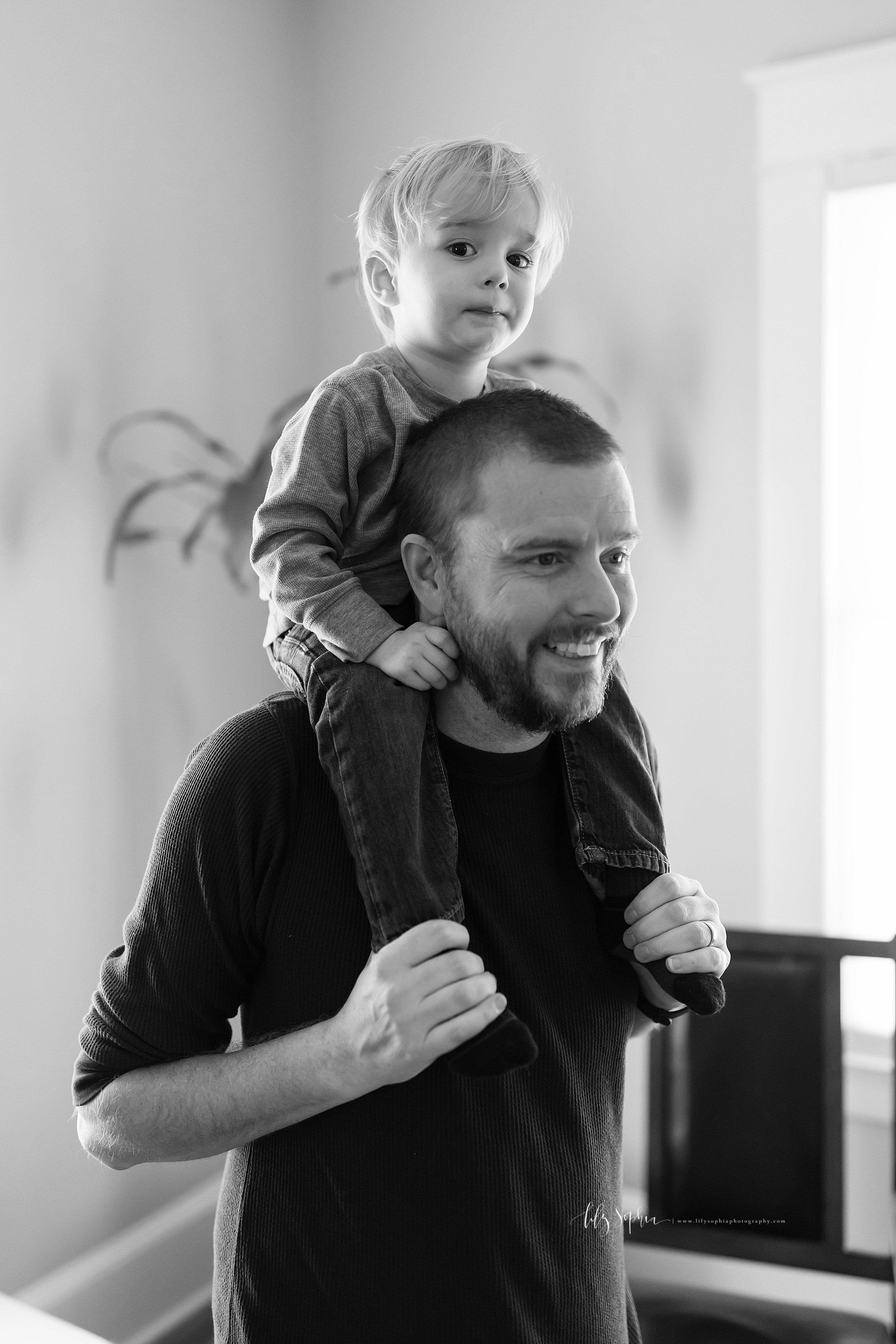  Black and white lifestyle photo of a toddler riding on the shoulders of his dad in his home in Atlanta in natural light. 