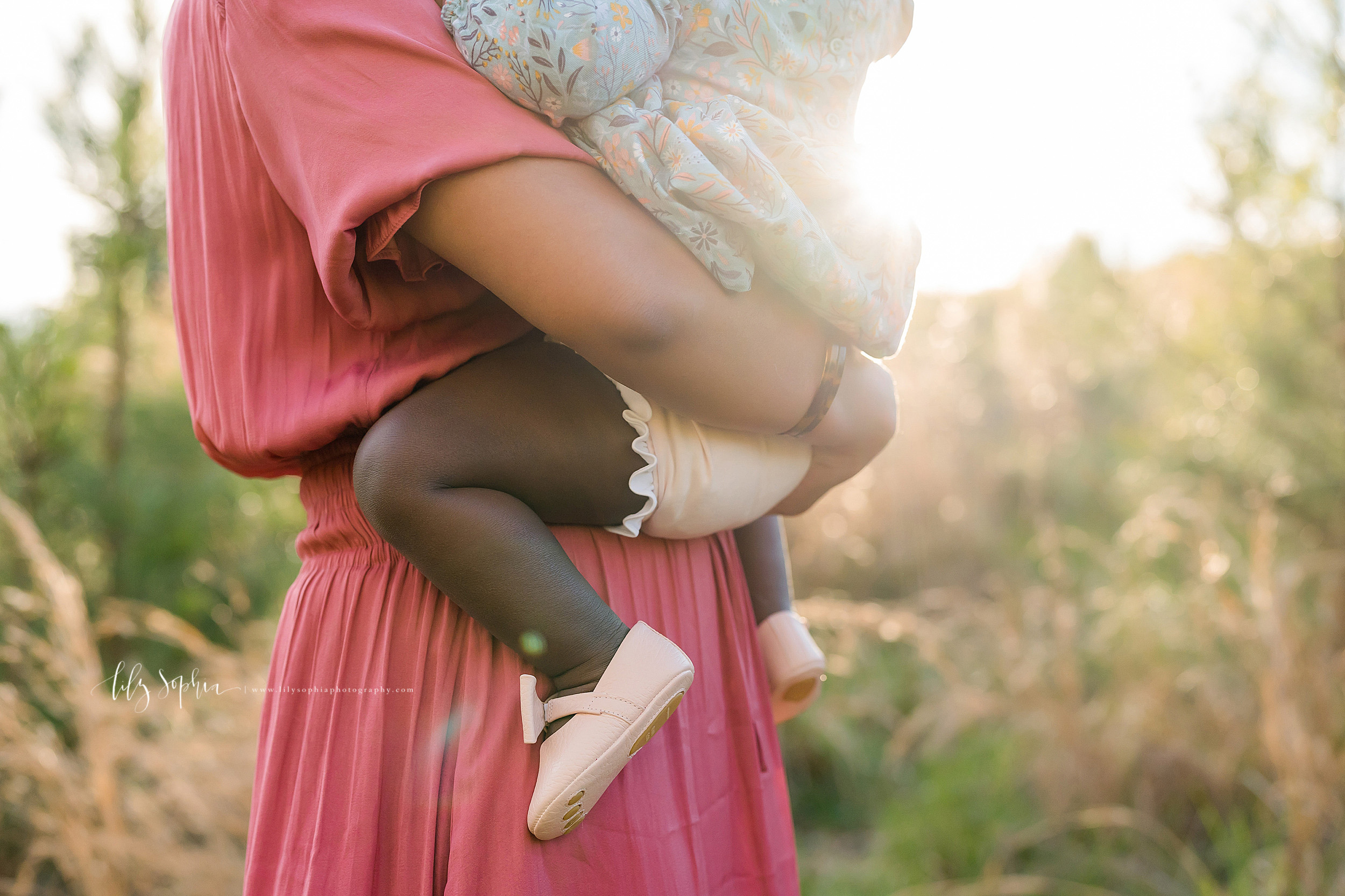  Milestone photo of a one year old’s chubby legs and feet as her mother holds her daughter in a field in Atlanta at sunset.  The African-American baby girl is wearing pink ballet shoes and a pink ruffled diaper cover.  Precious memories of being one.