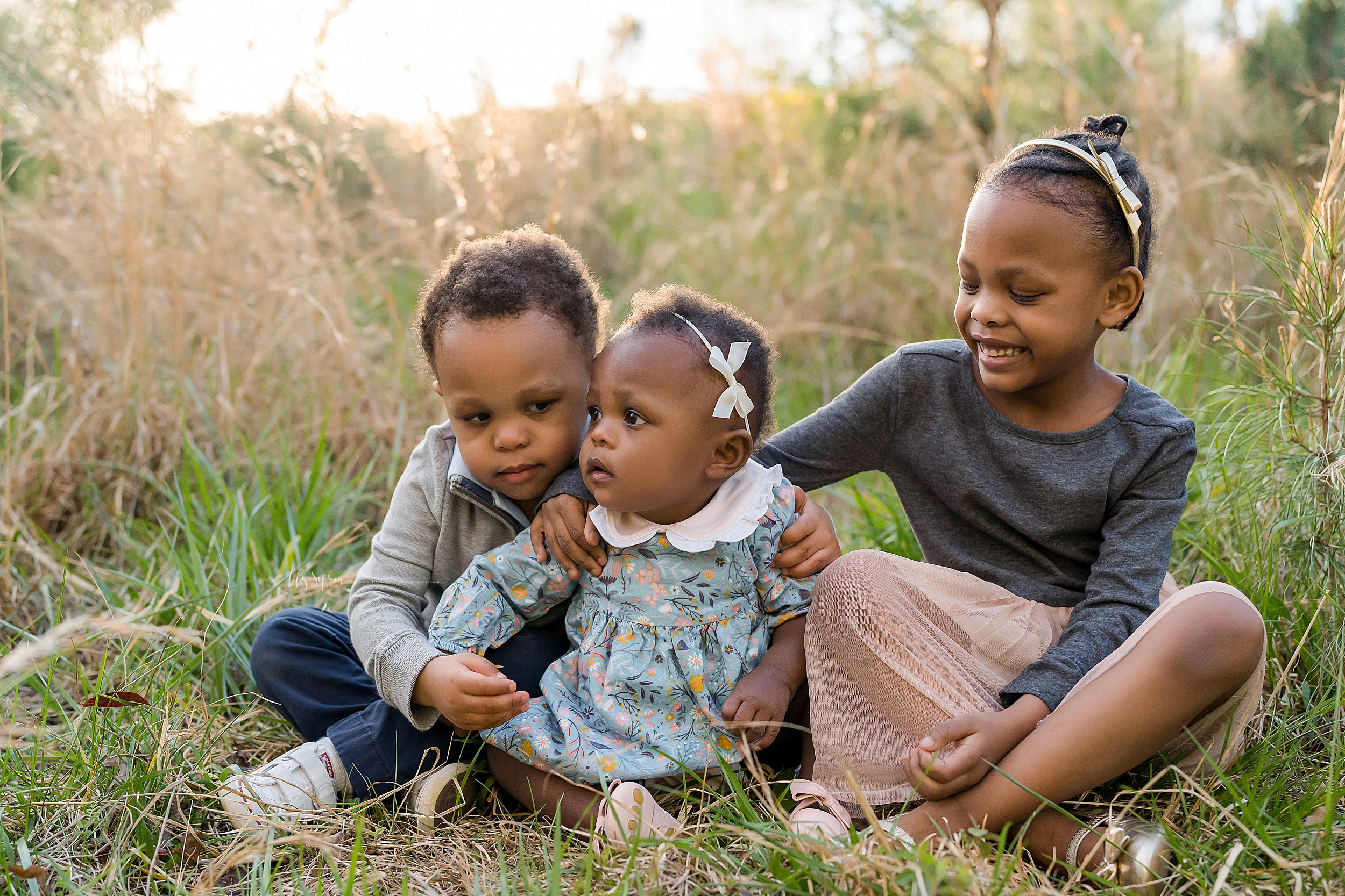  Photo of African-American siblings as their sister turns one.  The three children are sitting in a field at sunset in Atlanta.  The photo was taken by Lily Sophia Photography. 