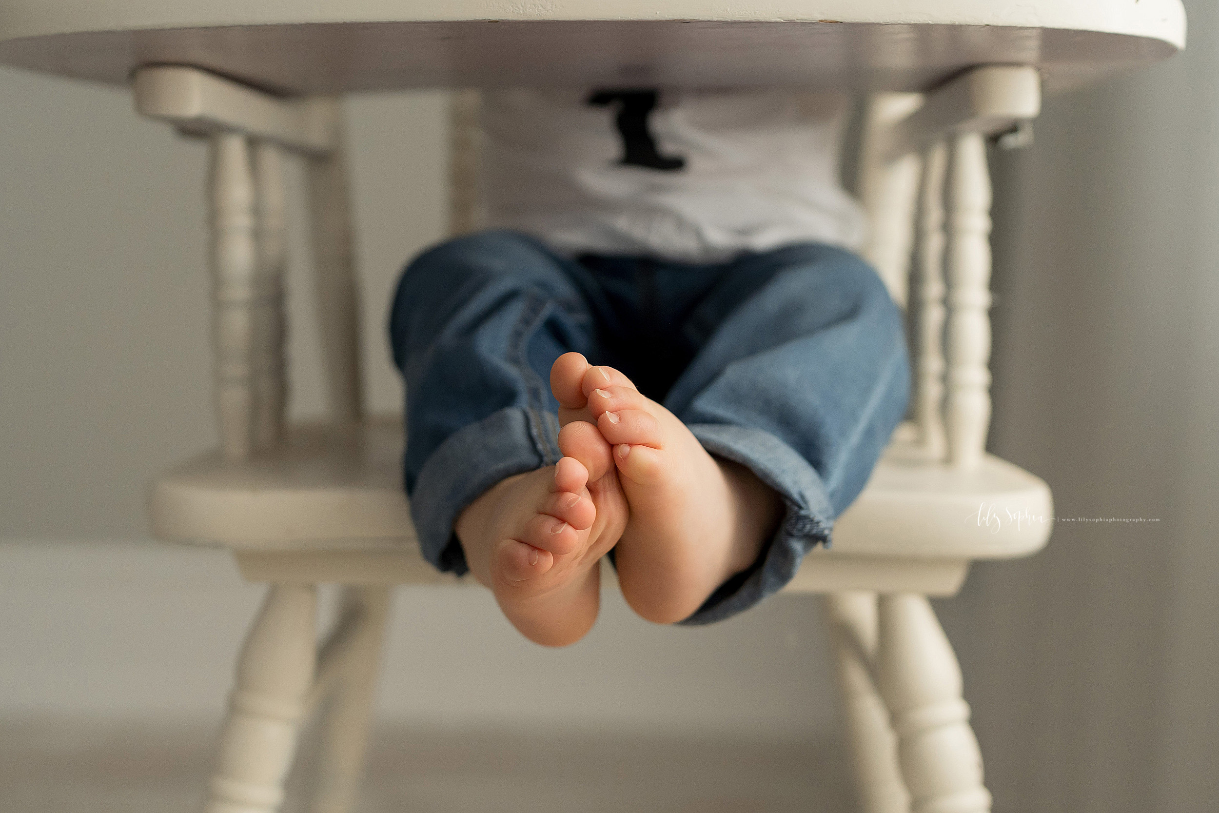 Milestone image of a one-year old as he sits in an antique high chair. The photo shows his sweet legs and feet.
