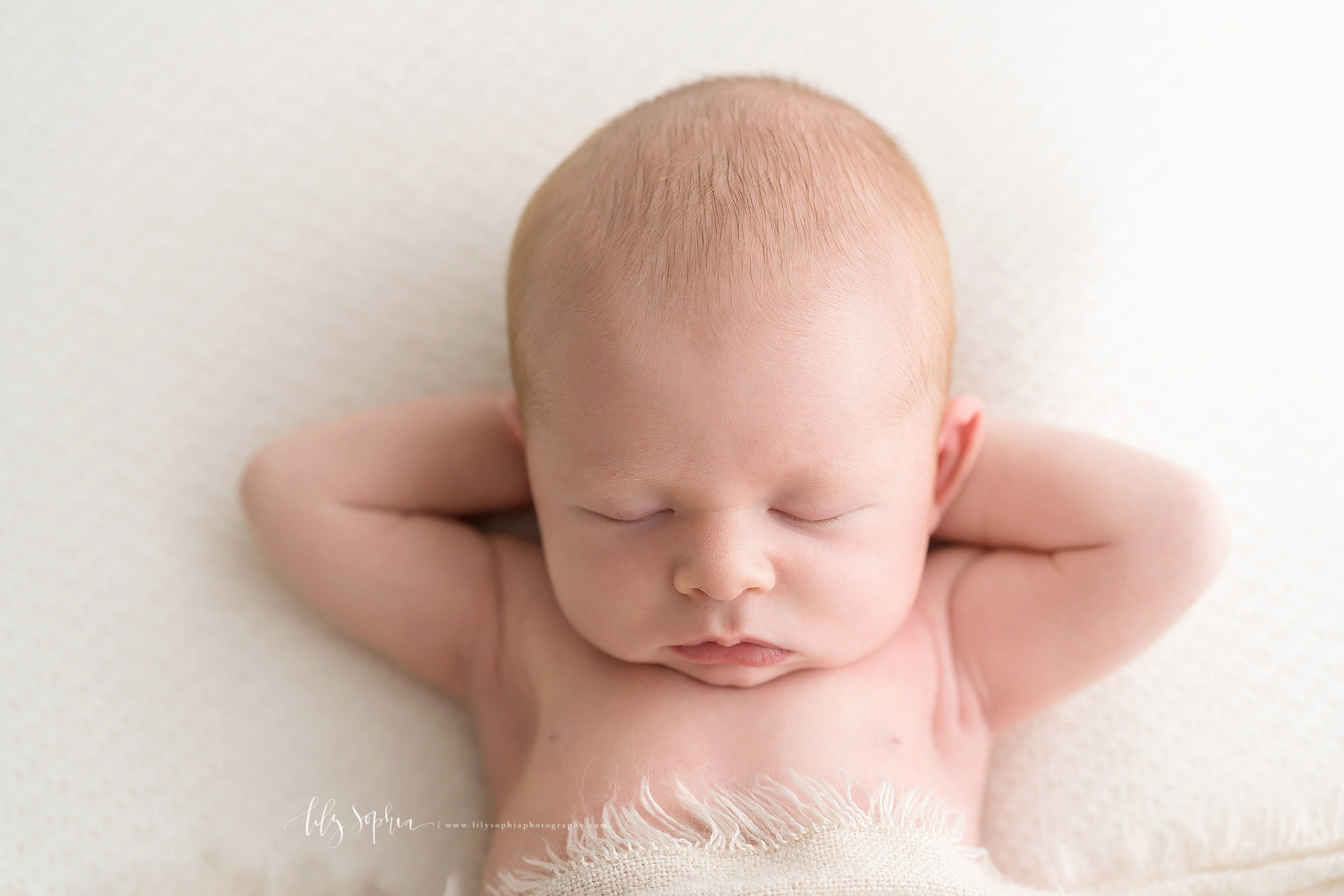 Newborn photo of a baby boy chilling in Atlanta with his hands behind his head as he sleeps in a natural light studio.