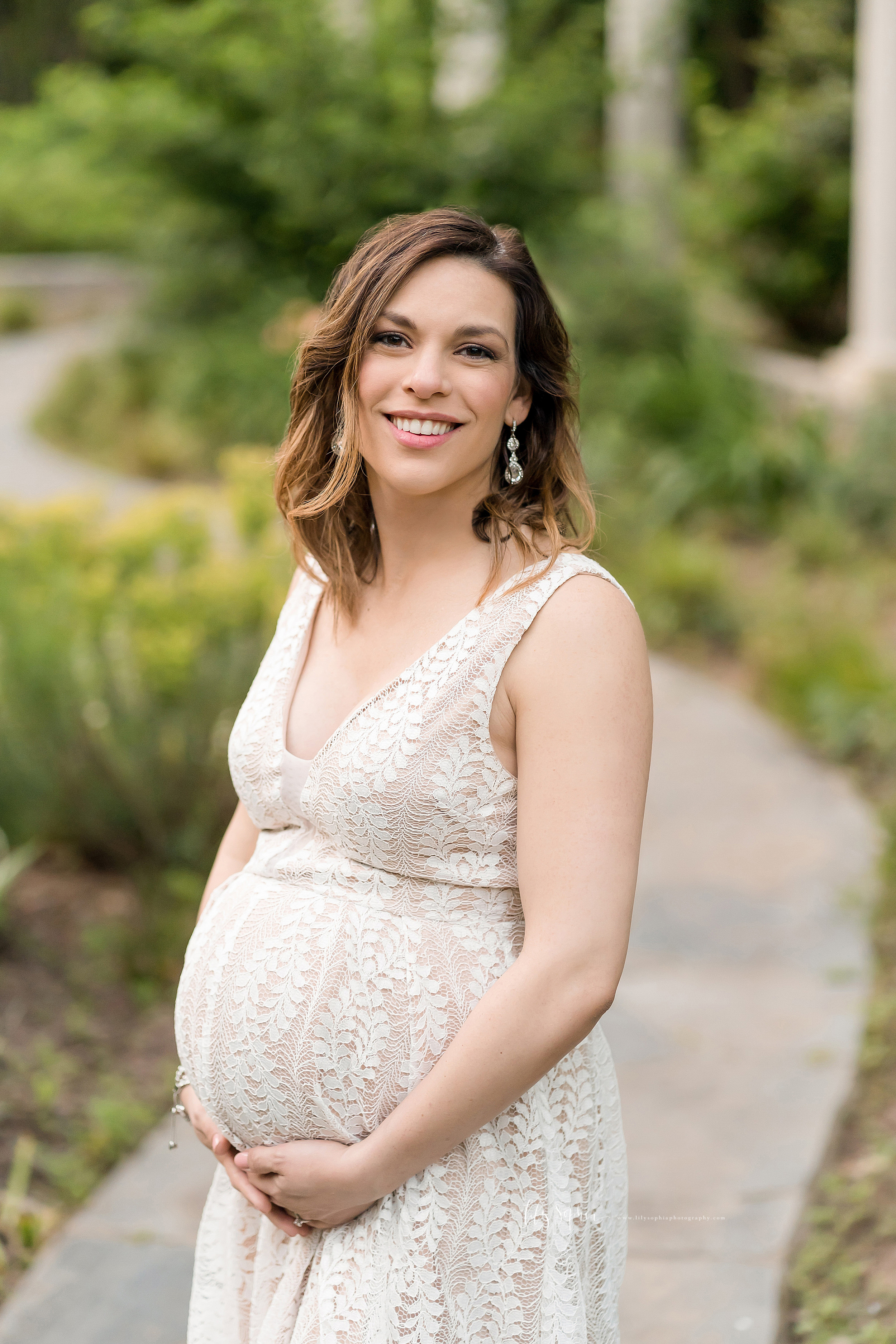  Maternity photo of a woman standing on a winding path in an Atlanta garden at sunset. 