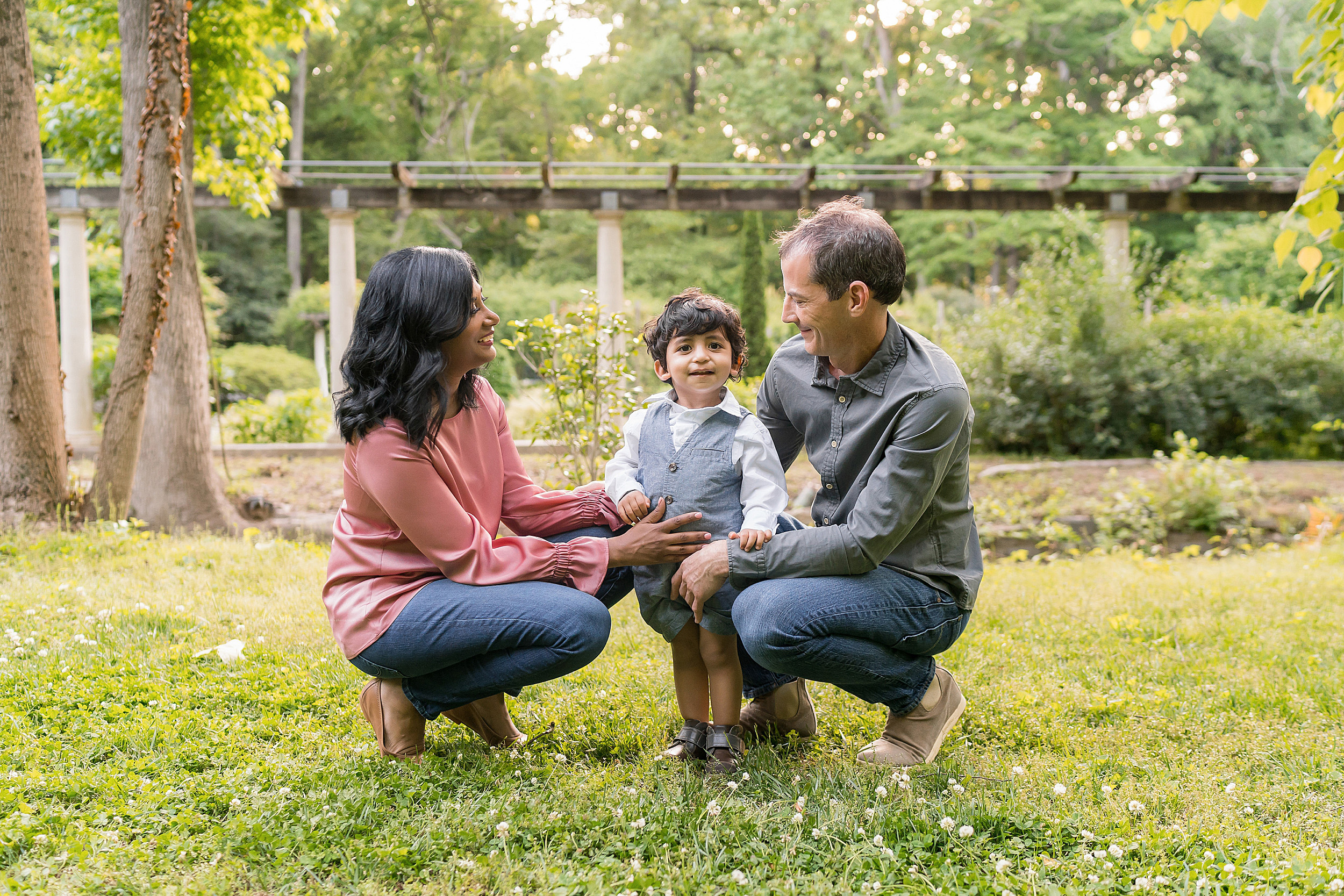  Photo of a family of three as mom and dad squat in a garden with their son standing between them at sunset in Atlanta. 