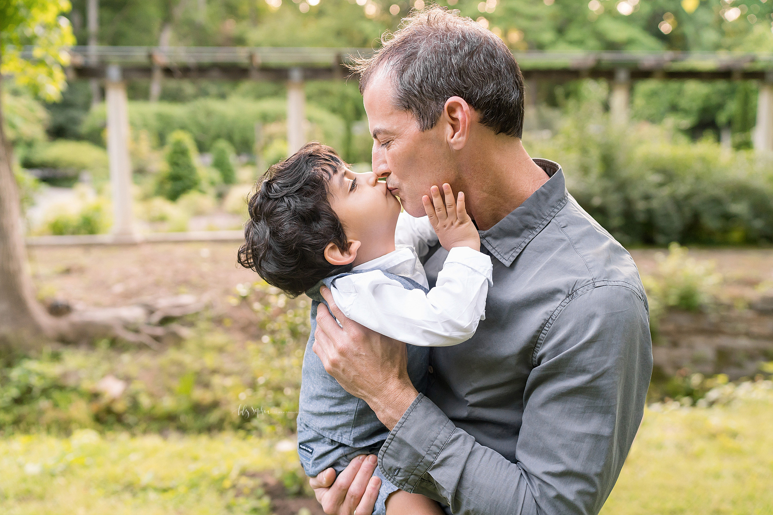  Family photo of a boy and his father as they kiss one another in an Atlanta garden at sunset. 