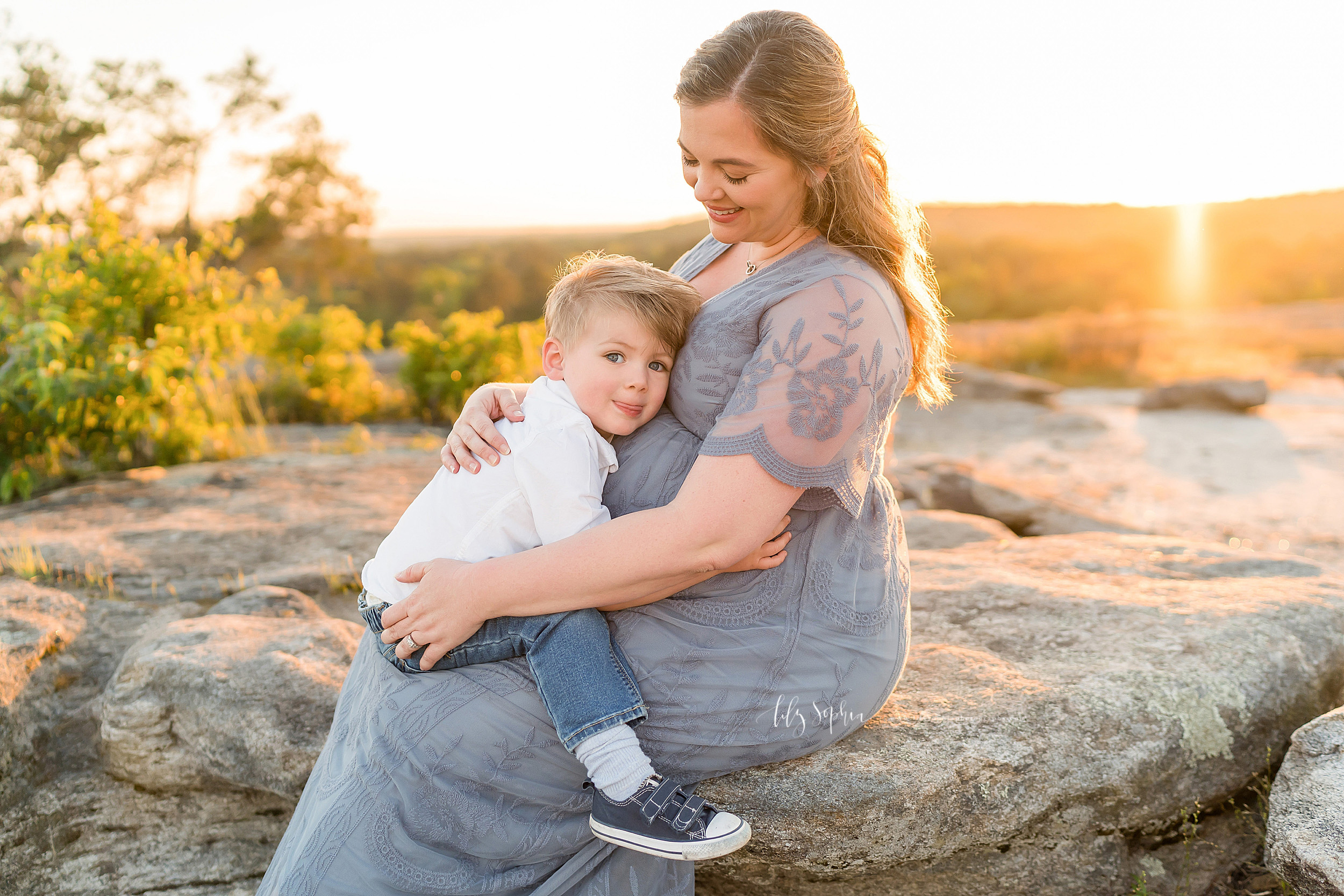  Photo of a pregnant mother holding her toddler son on her lap as she sits on a stone mountaintop near Atlanta, GA. 