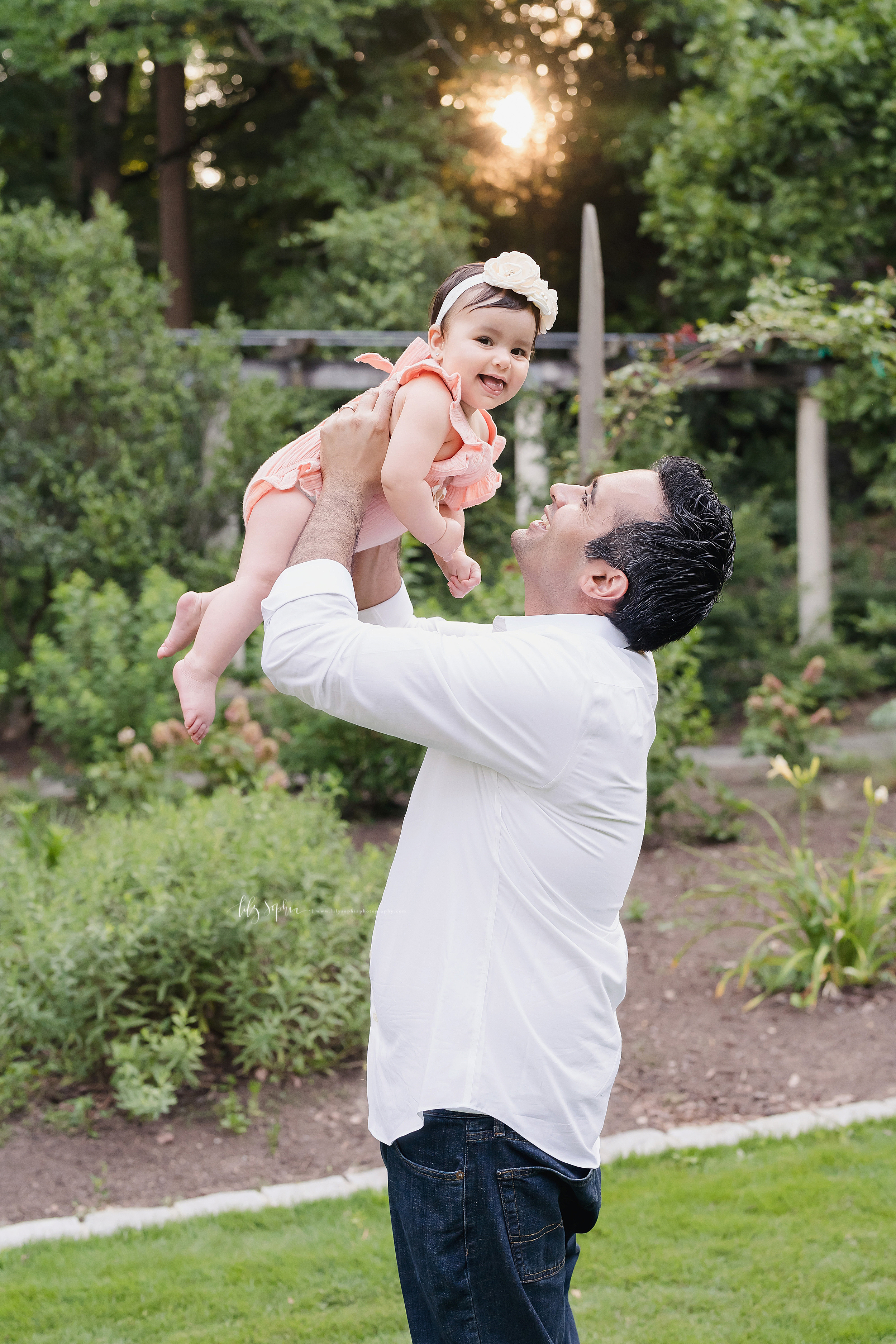  Photo of a dad and his daughter at sunset as he holds his daughter over his head in a garden in Atlanta. 