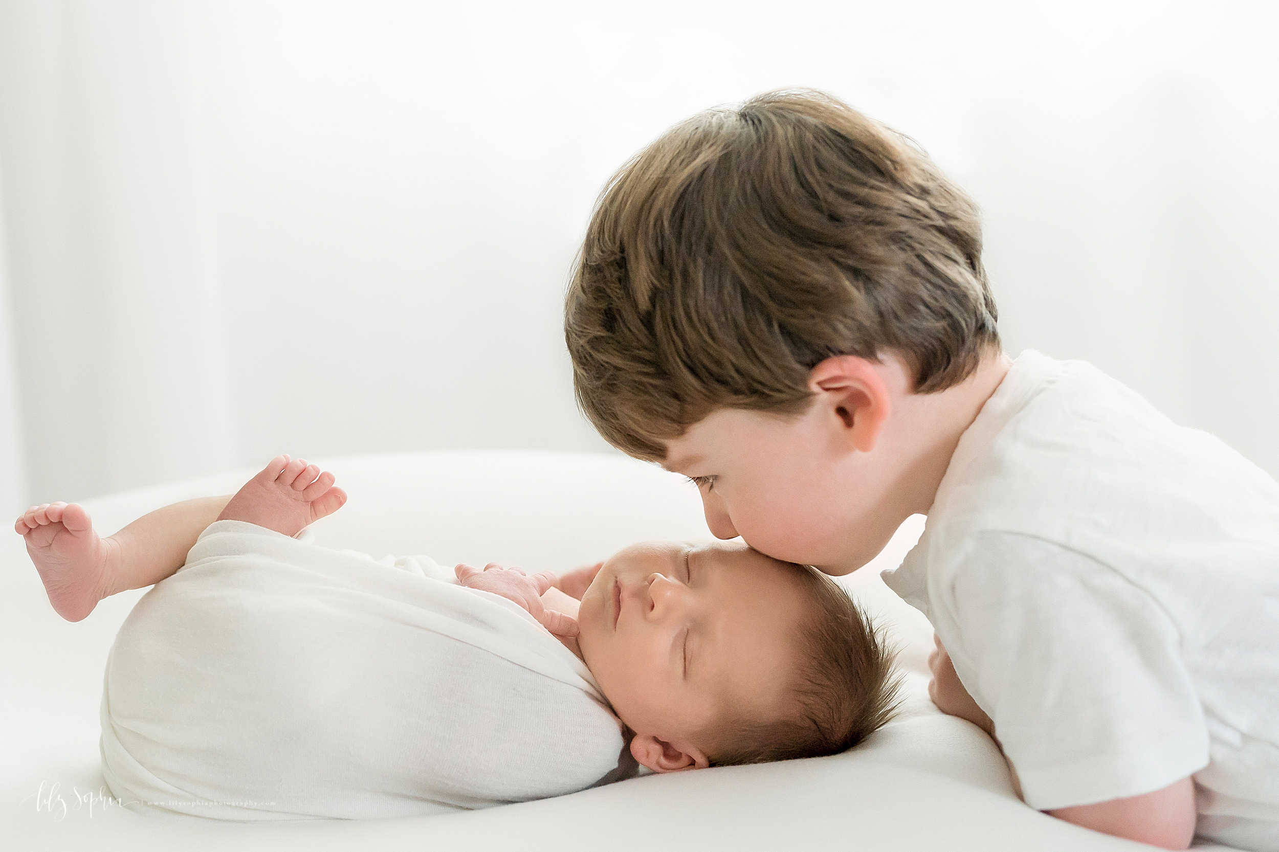  Newborn photo of a sleeping baby boy and his big brother as his brother kisses him on his head in Atlanta in natural light. 