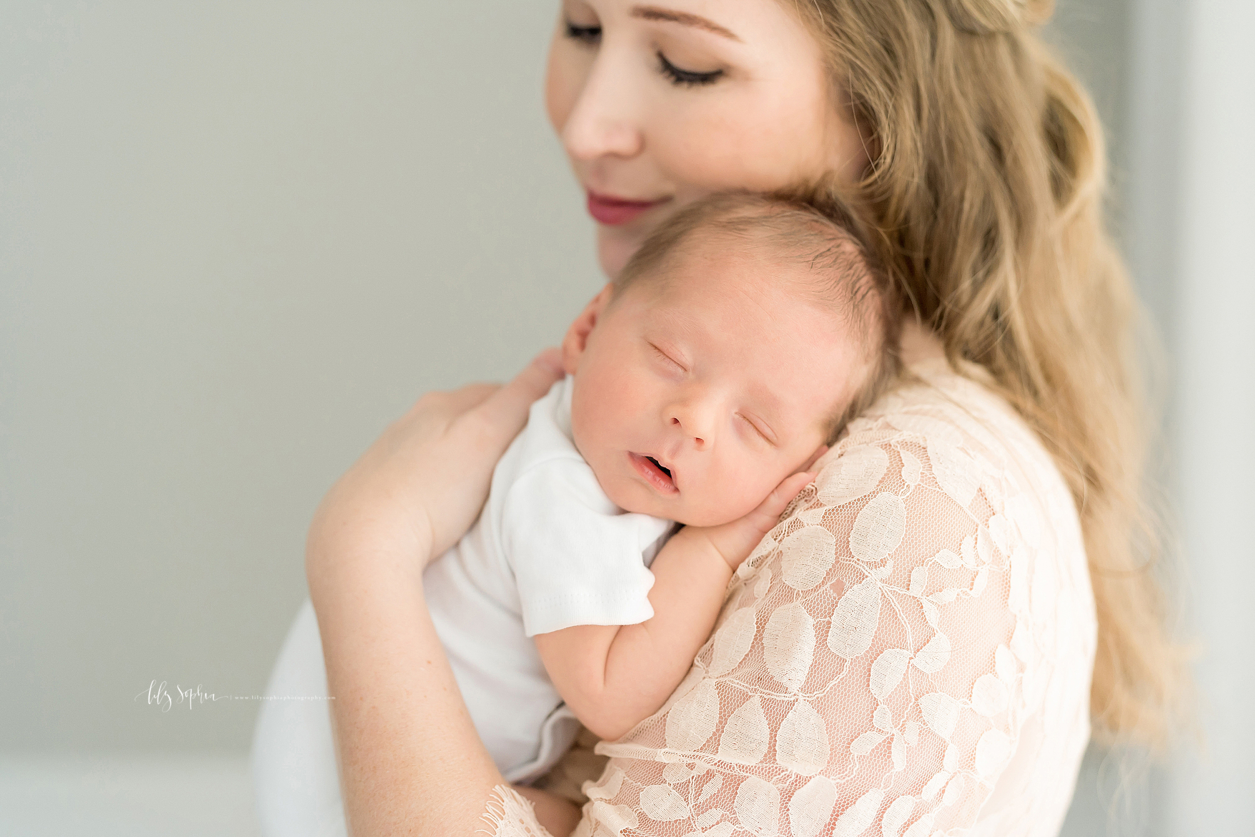  Newborn photo of a blonde haired mother holding her sleeping infant son on her shoulder as she stands in Atlanta in a studio using natural light. 