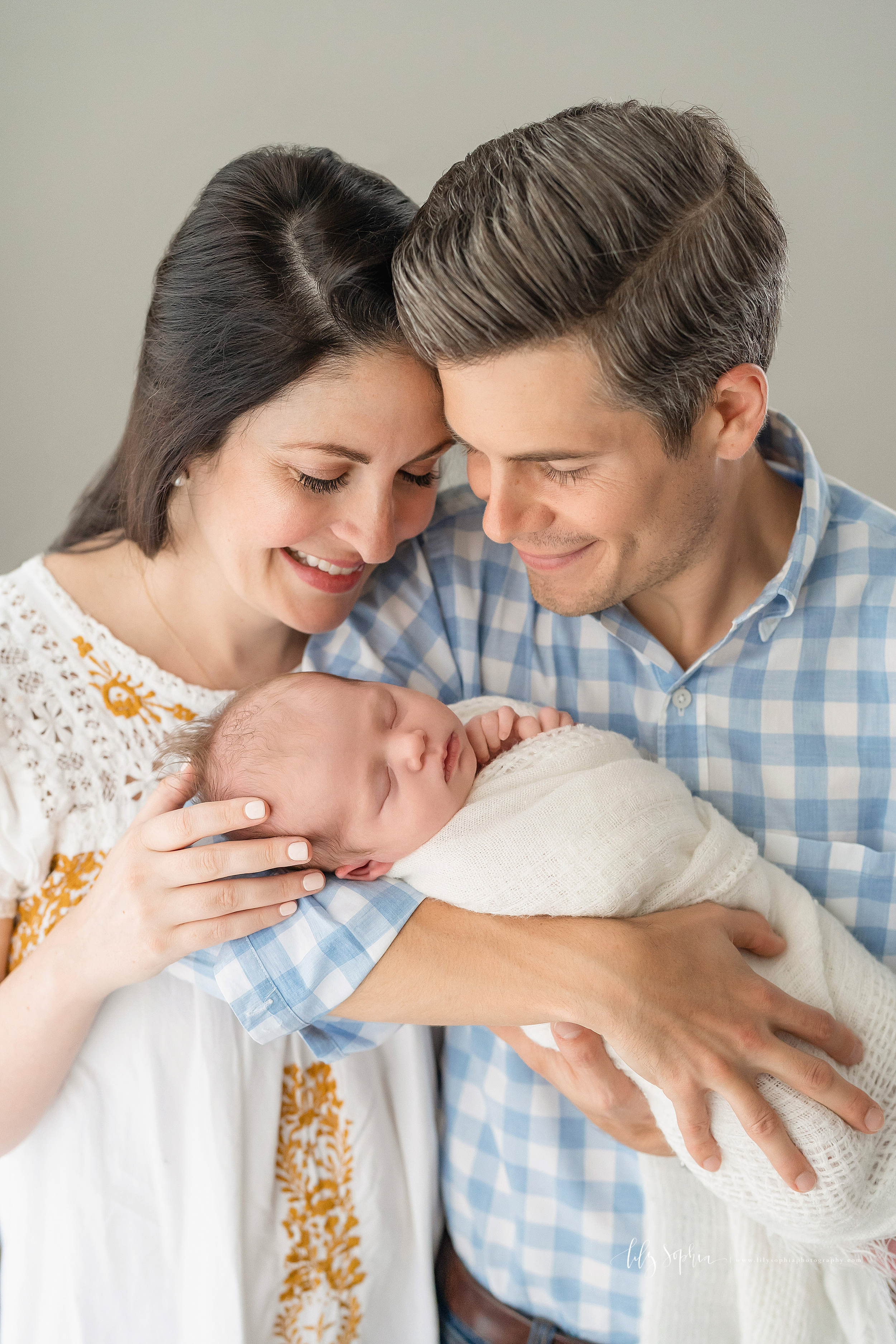  Family photo of three, mom, dad and their newborn daughter, as the parents admire their sleeping baby daughter in an Atlanta studio. 