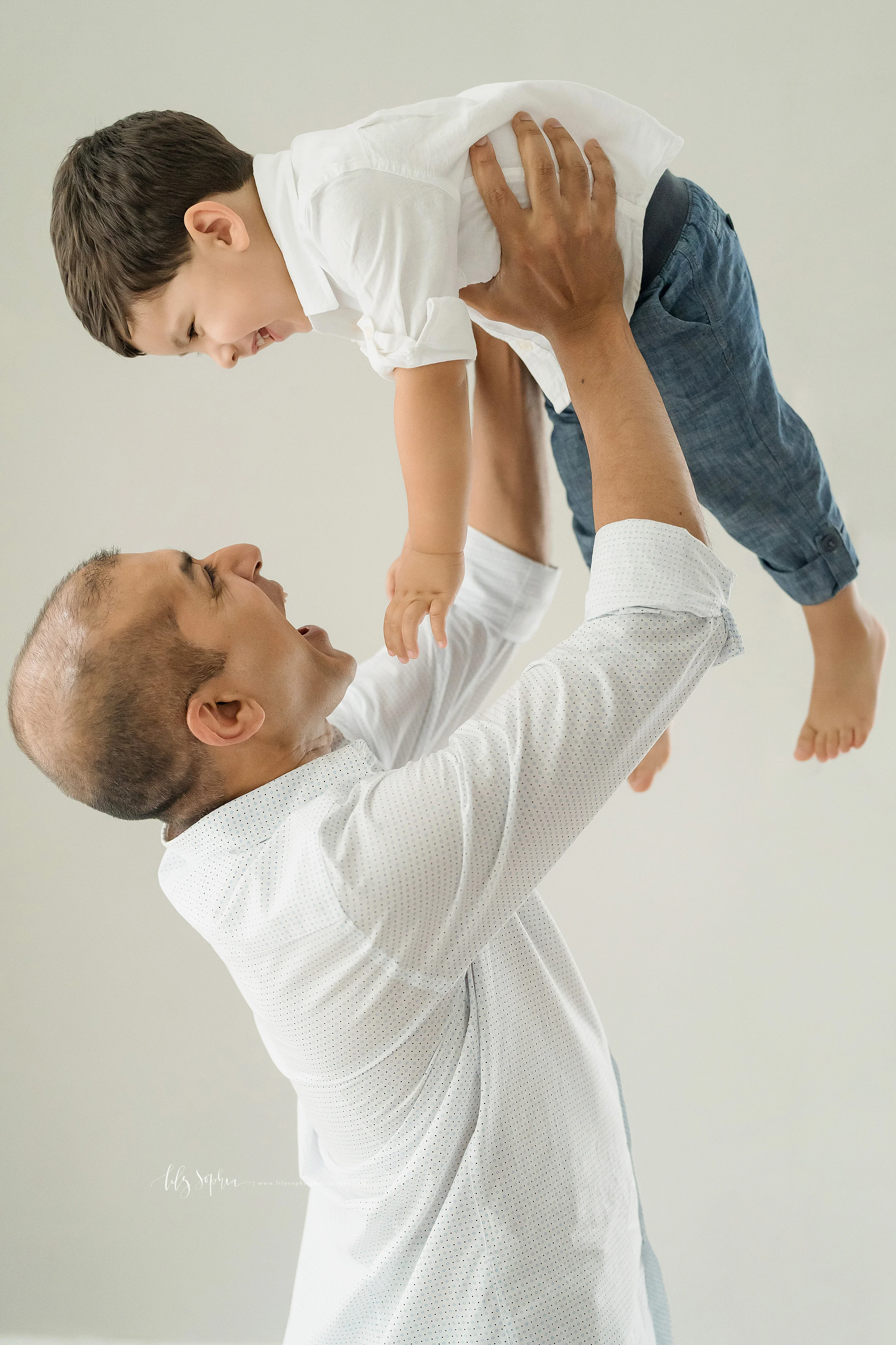 Family photo of a father lifting his son above his head as the two laugh together in an Atlanta studio.