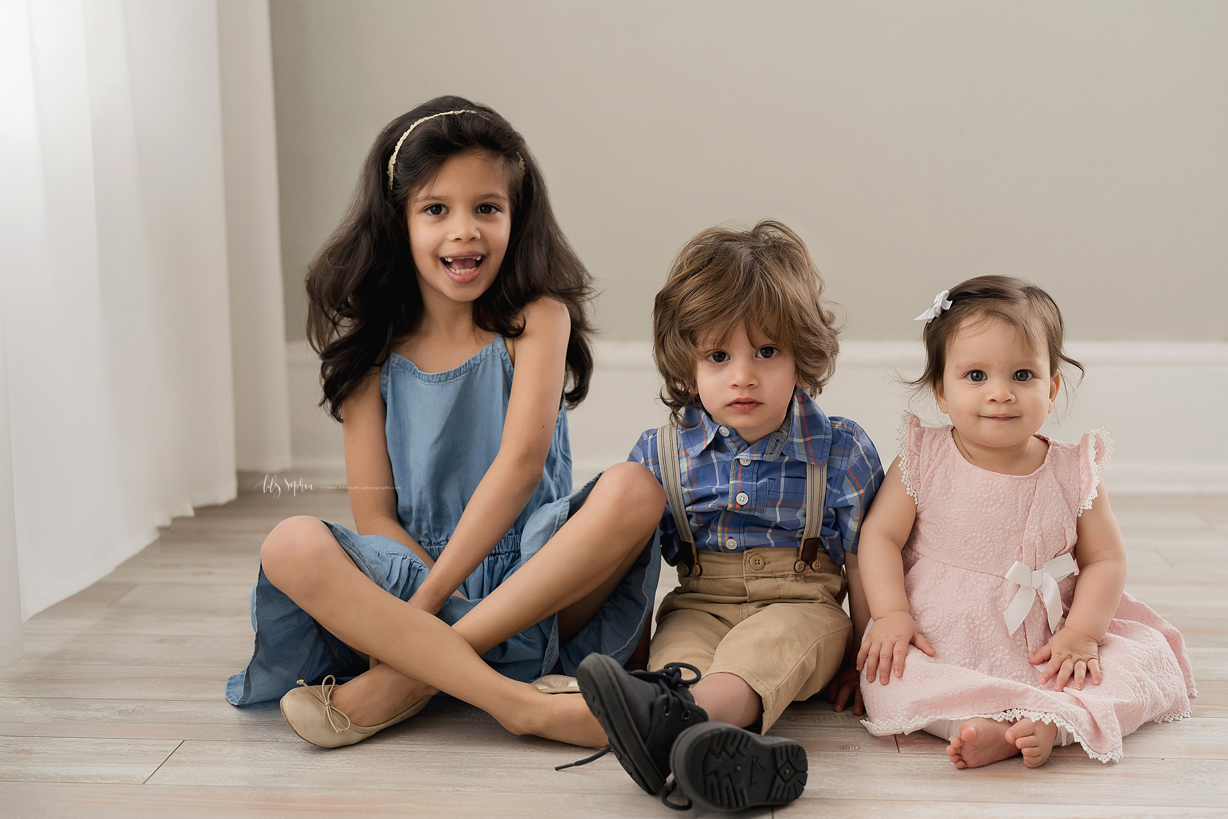  Family photo of a brother sitting between his two sisters on the floor of a natural light Atlanta studio. 