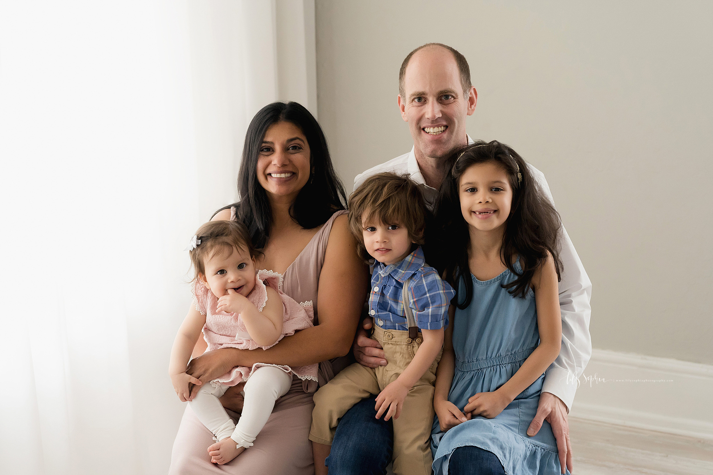  Family photo of five sitting in front of a natural light window in an Atlanta studio, mom, nine month old daughter, toddler son, older daughter, and the father. 