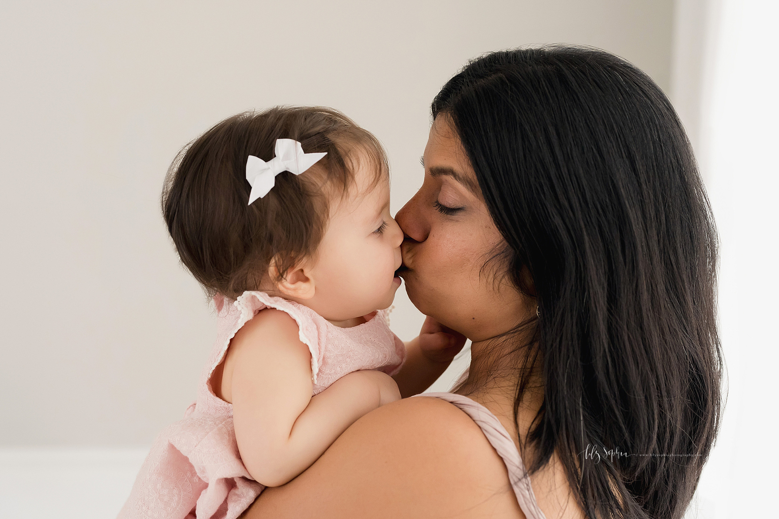  Milestone photo of a mom holding her nine month old daughter in a studio in Atlanta as they kiss one another in natural light. 