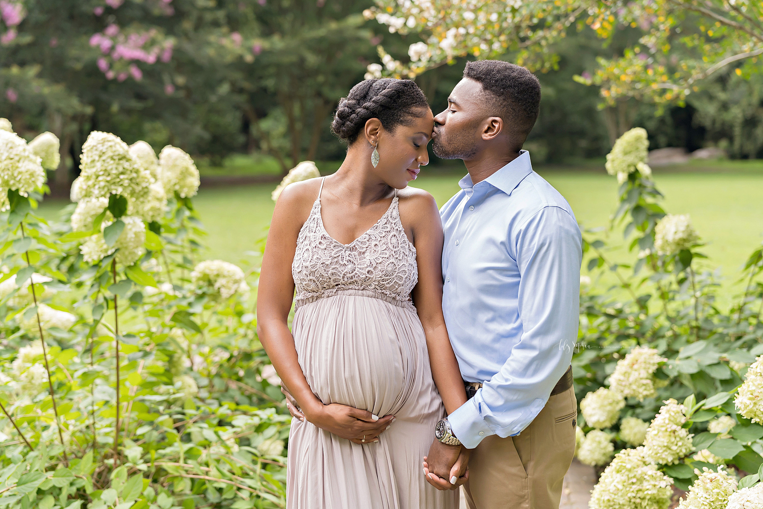  Photo of an expectant African-American couple as they stand in an Atlanta garden holding hands and the husband kisses the forehead of his pregnant wife. 