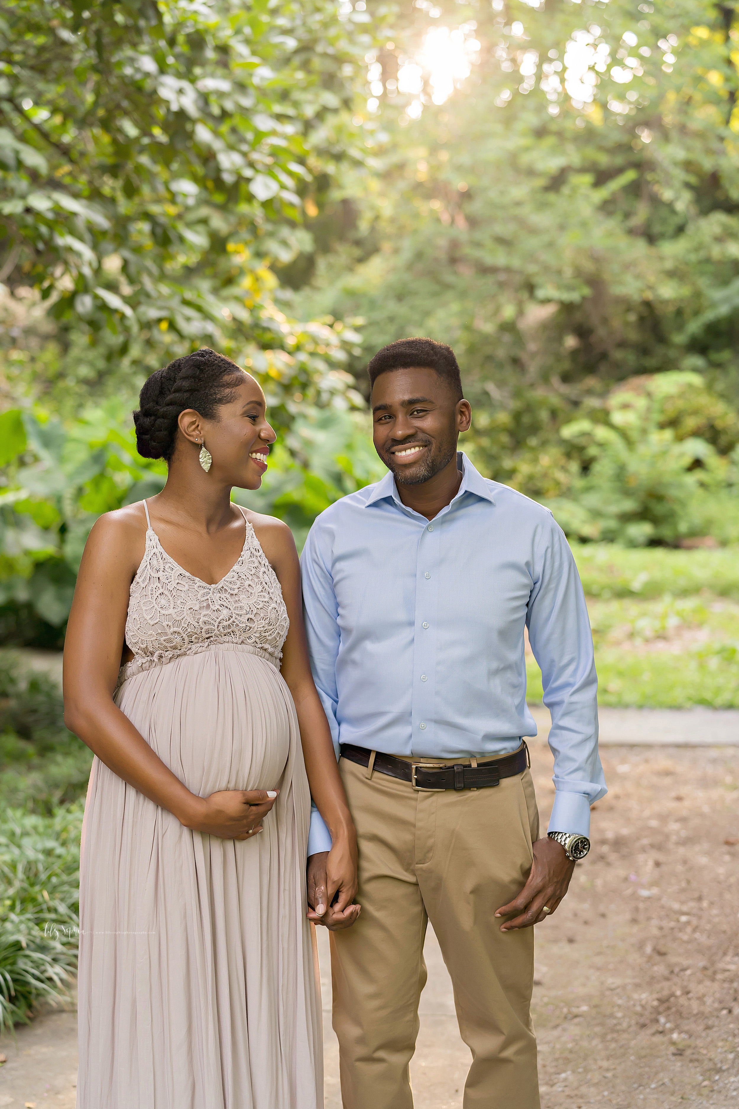  Maternity photo of a happy African-American couple as they stand hand in hand in an Atlanta garden at sunset. 