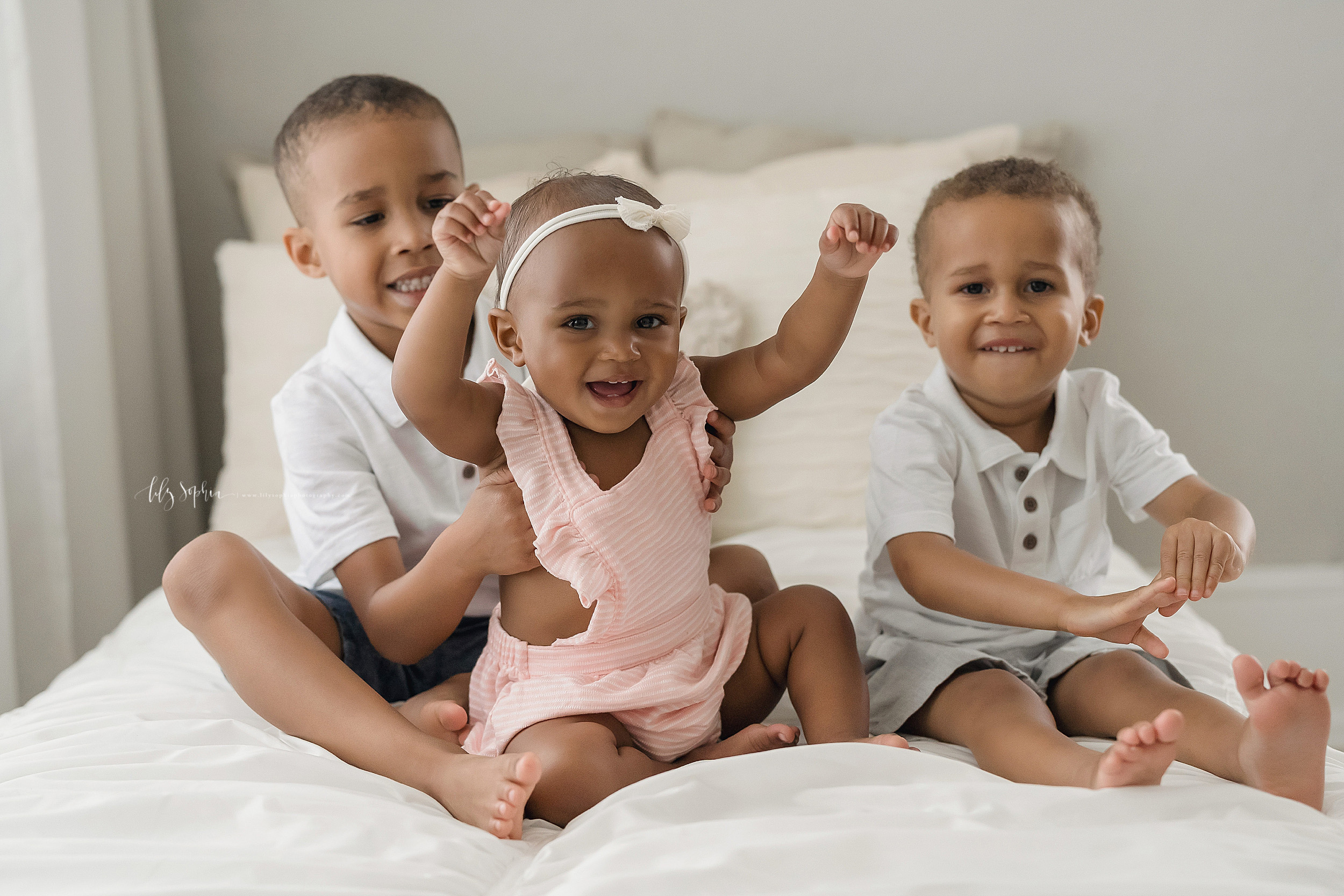  Family photo of African-American brothers with their one year old sister as they sit on a bed in an Atlanta natural light studio. 